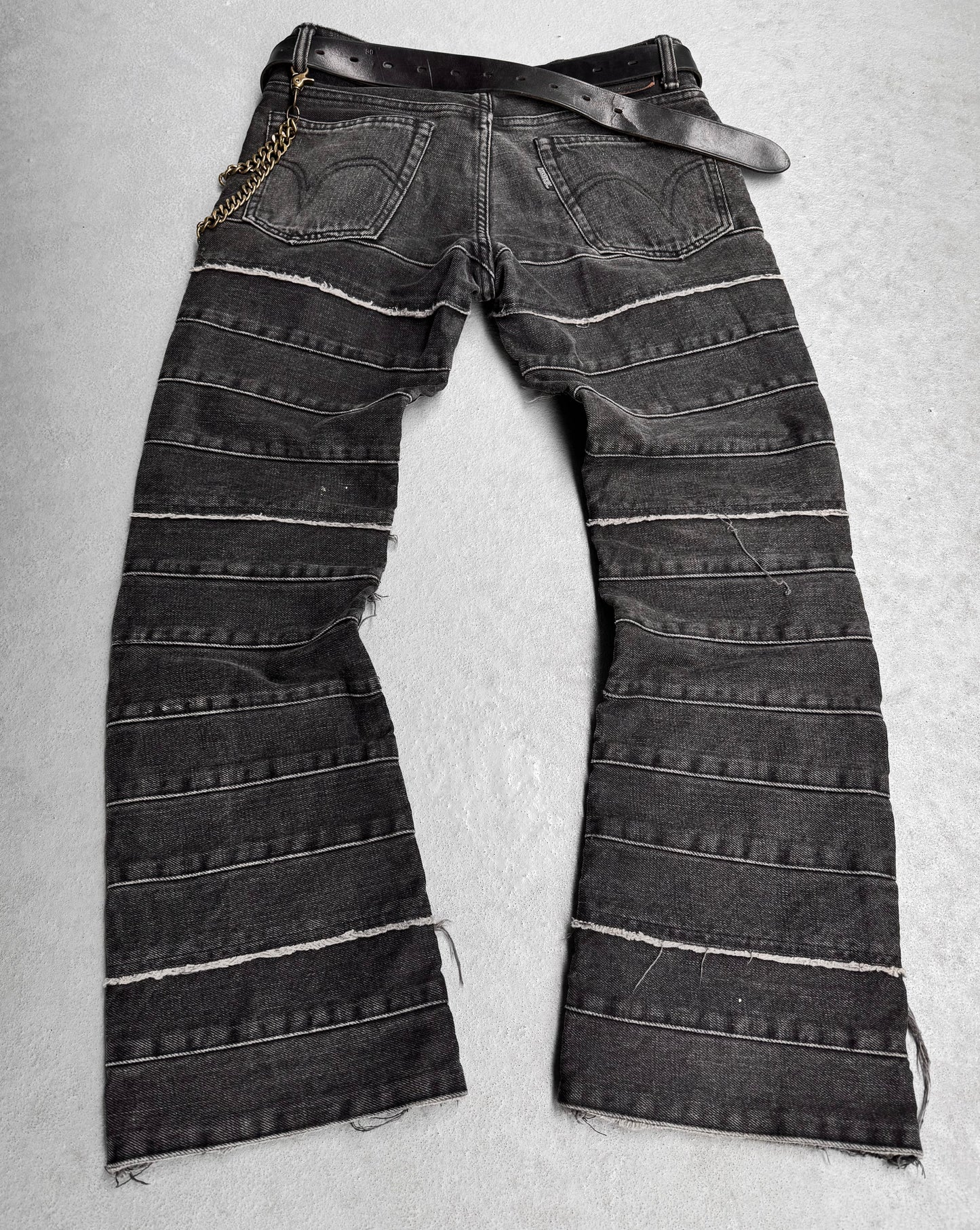 Hysteric Glamours Early 00s ‘Kinky’ Grey Flare Hagi Denim showcases punk rock fashion with distressed stripes, a frayed hem, and a gold chain-attached black belt, displayed on a light floor.
