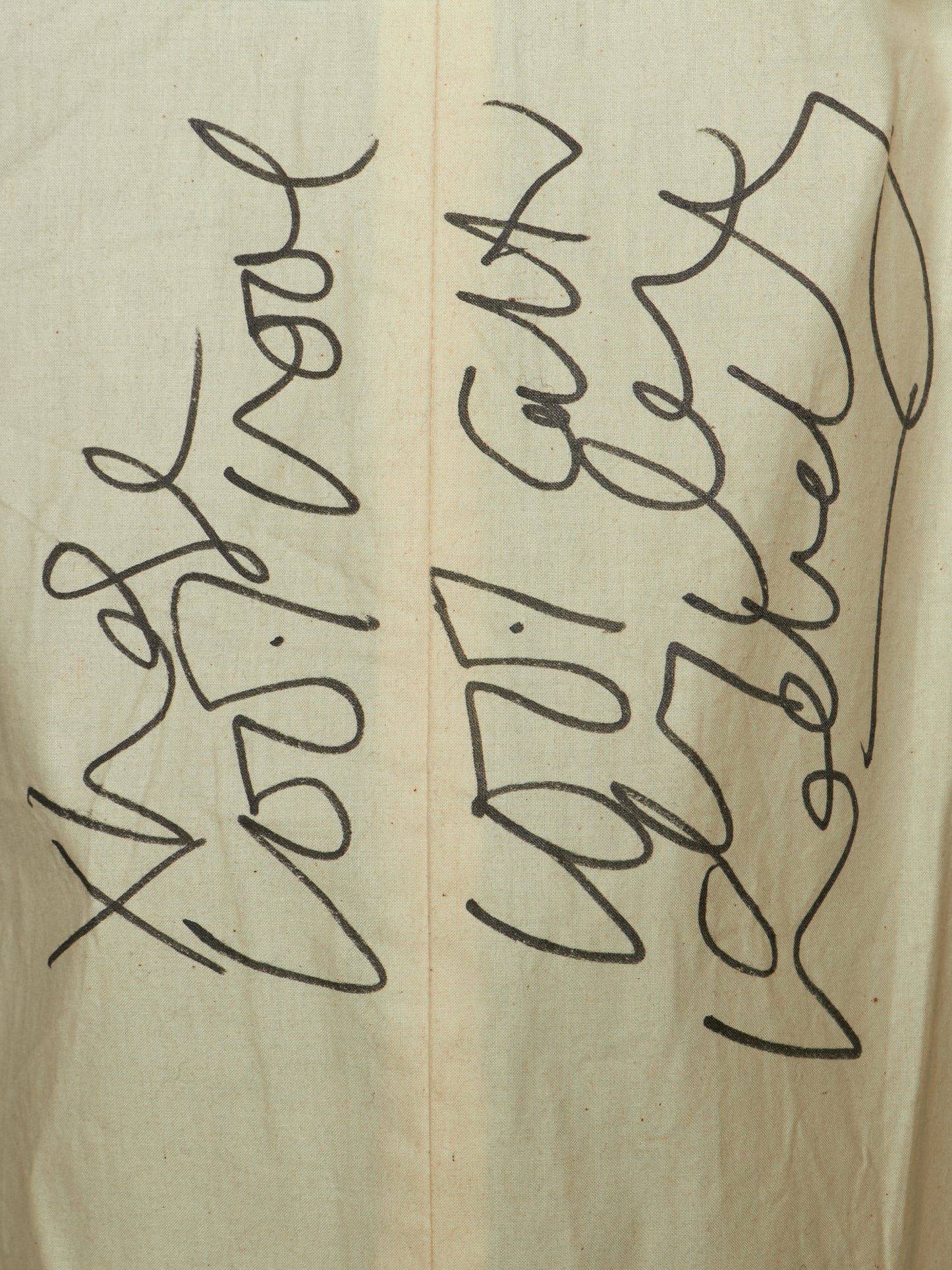 A close-up of a beige fabric surface with black handwritten or printed abstract script running vertically across it.