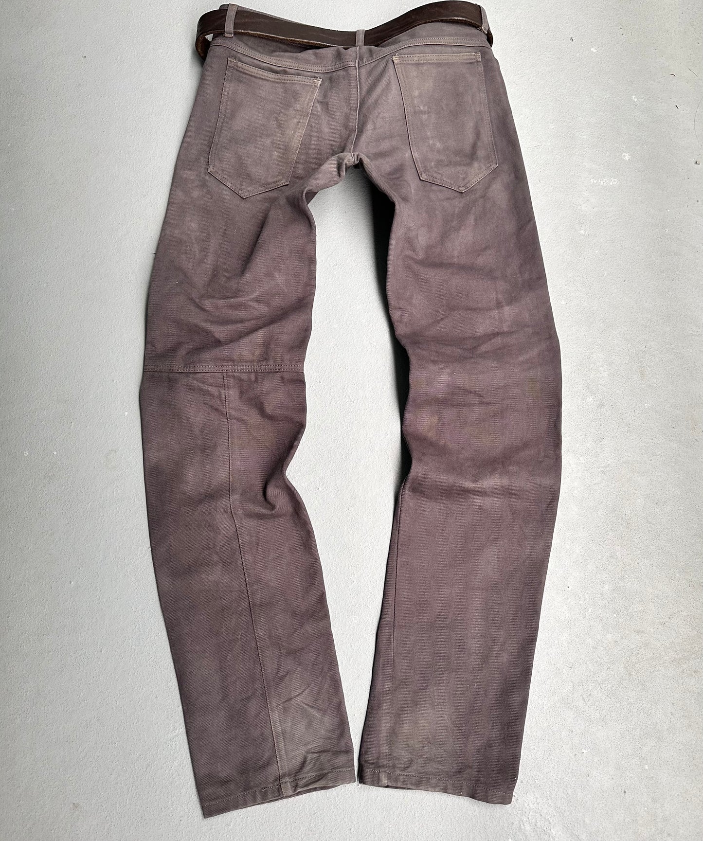 The ANDREW MACKENZIE Early 00s Stud Darted Knee Denim features a back view with worn, faded detailing on the legs and seat, plus subtle folded knee accents for an avant-garde touch, laid flat on a light gray surface.