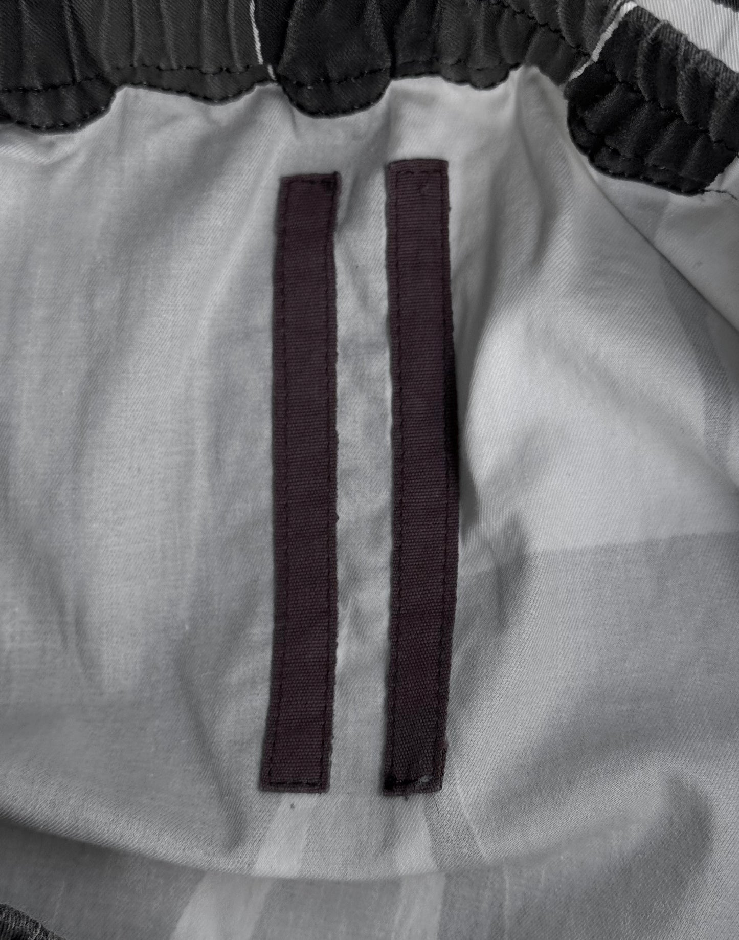 Close-up of the inner waistband of the Rick Owens DRKSHDW SS14 “VICIOUS” Geometric Camouflage Men’s Skirt, featuring two vertical black fabric strips sewn onto light gray material—a detail reflecting Rick Owens’ signature avant-garde style.