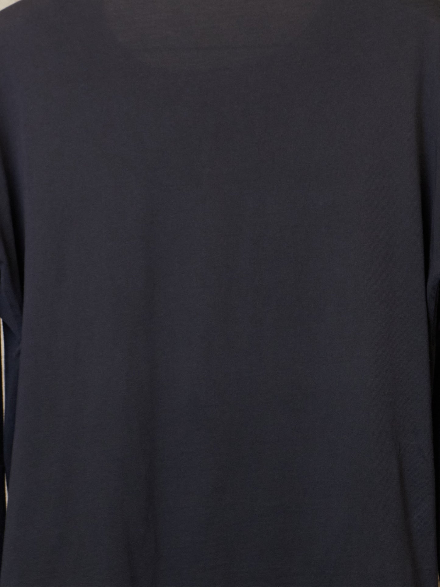Black long-sleeve shirt on a hanger against a textured beige wall.