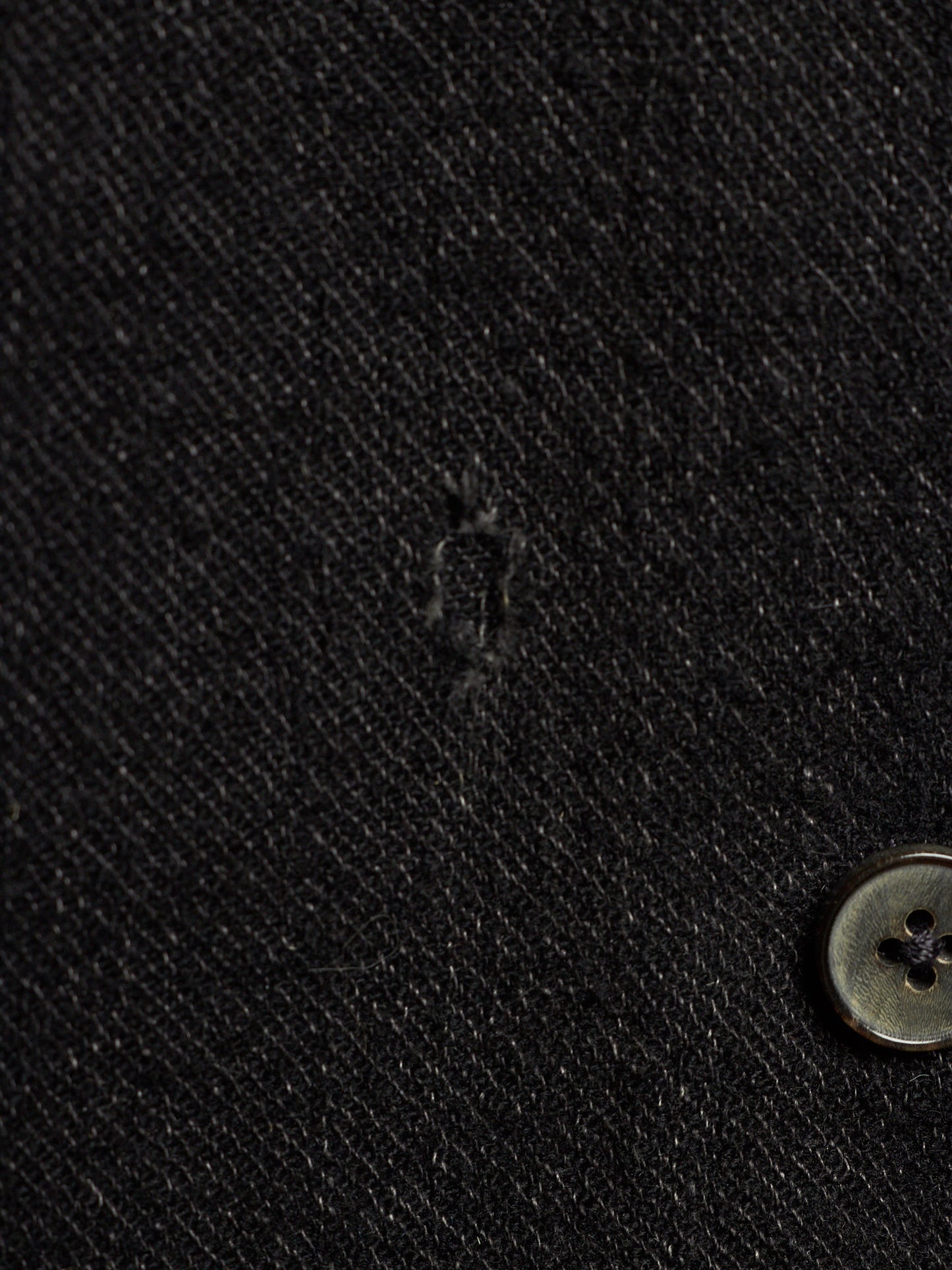 Close-up of a black textured fabric surface with a small button visible at the lower right.