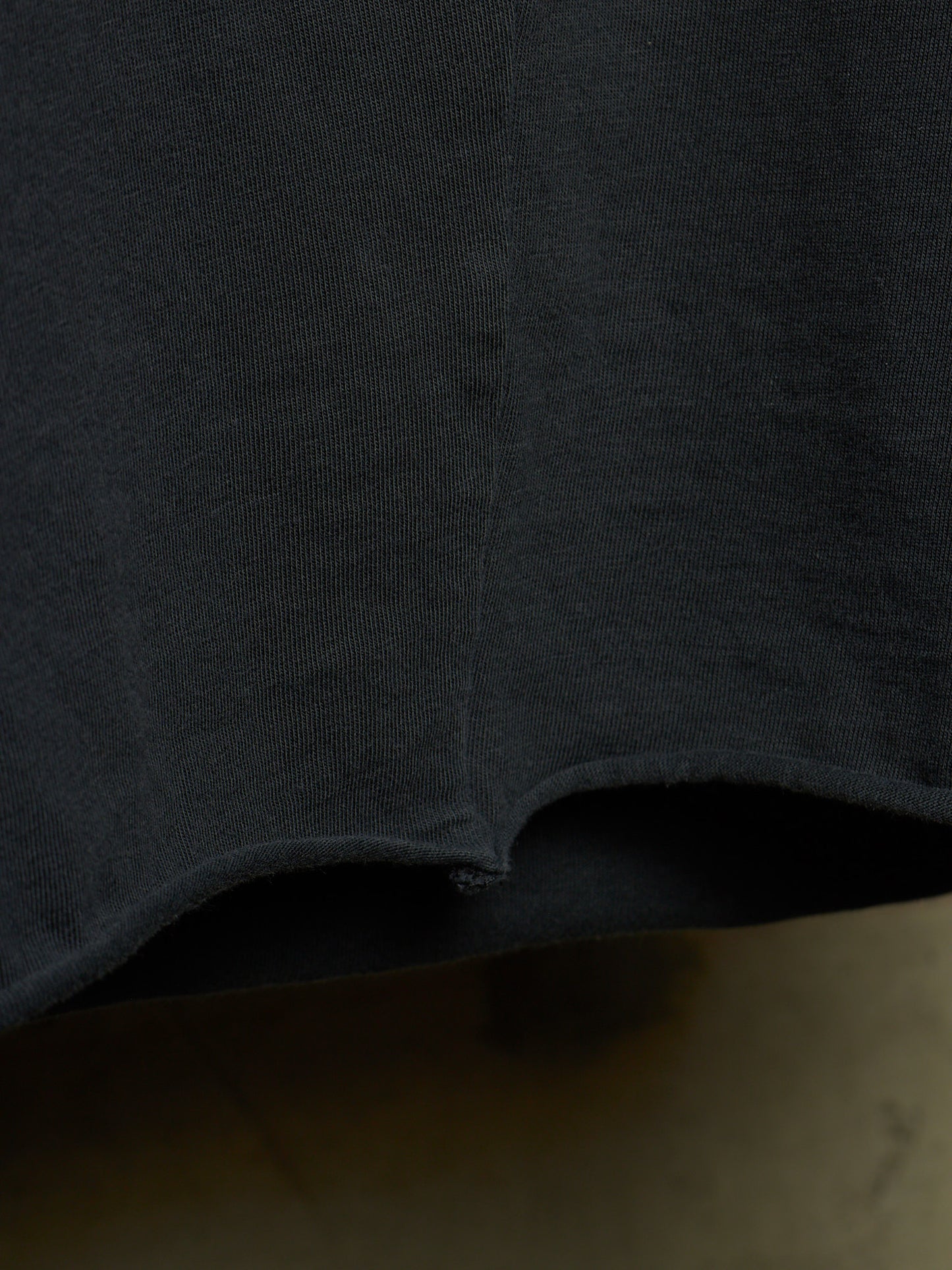 Close-up detail of a dark charcoal gray knit fabric garment, showing the texture and a curved hemline.