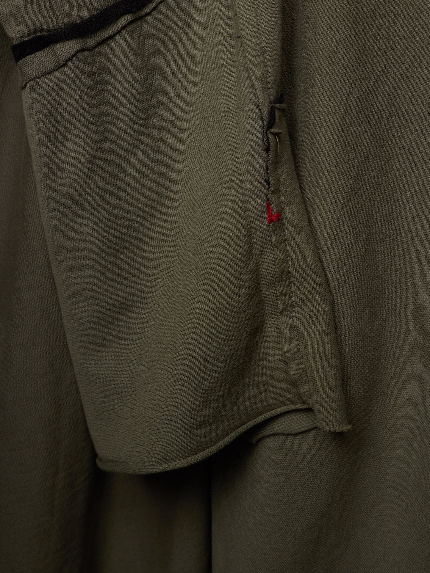 Close-up of olive green fabric with a small red accent stitch detail.