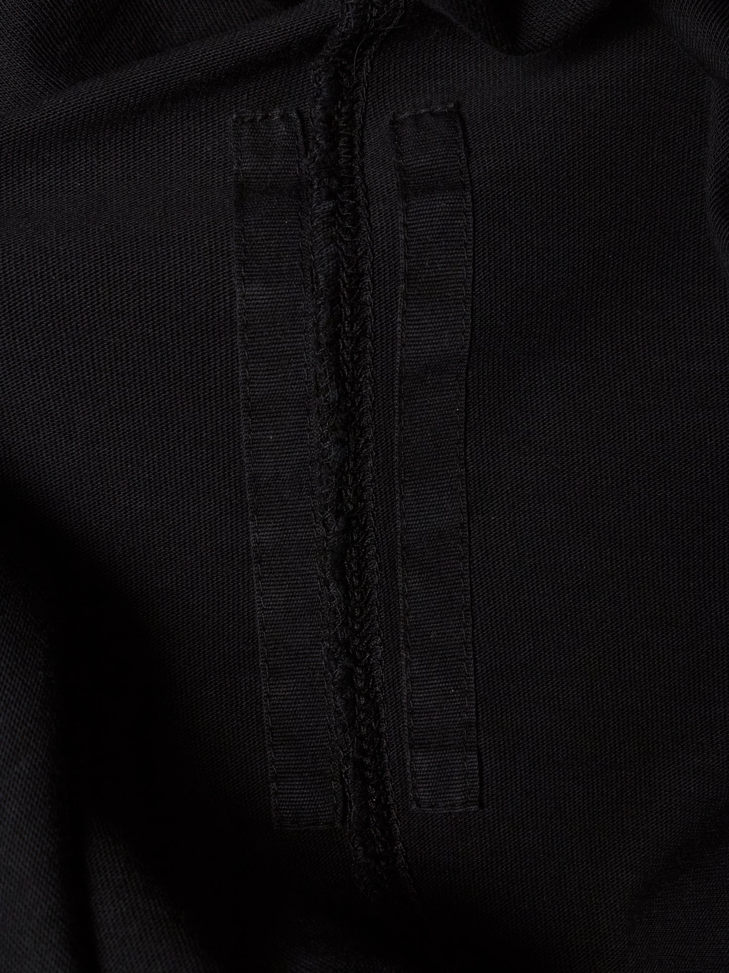 Close-up detail of a black textured fabric garment showing a central seam and a vertical stitched tab.
