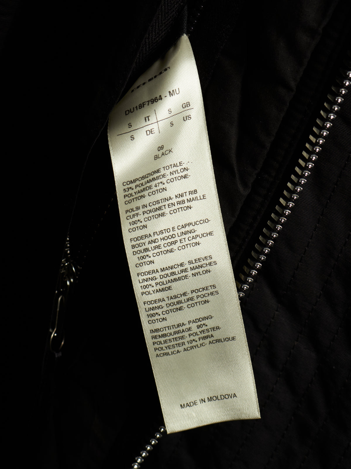 A close-up of a garment's interior showing a white paper size and care label sewn onto black fabric next to a zipper.