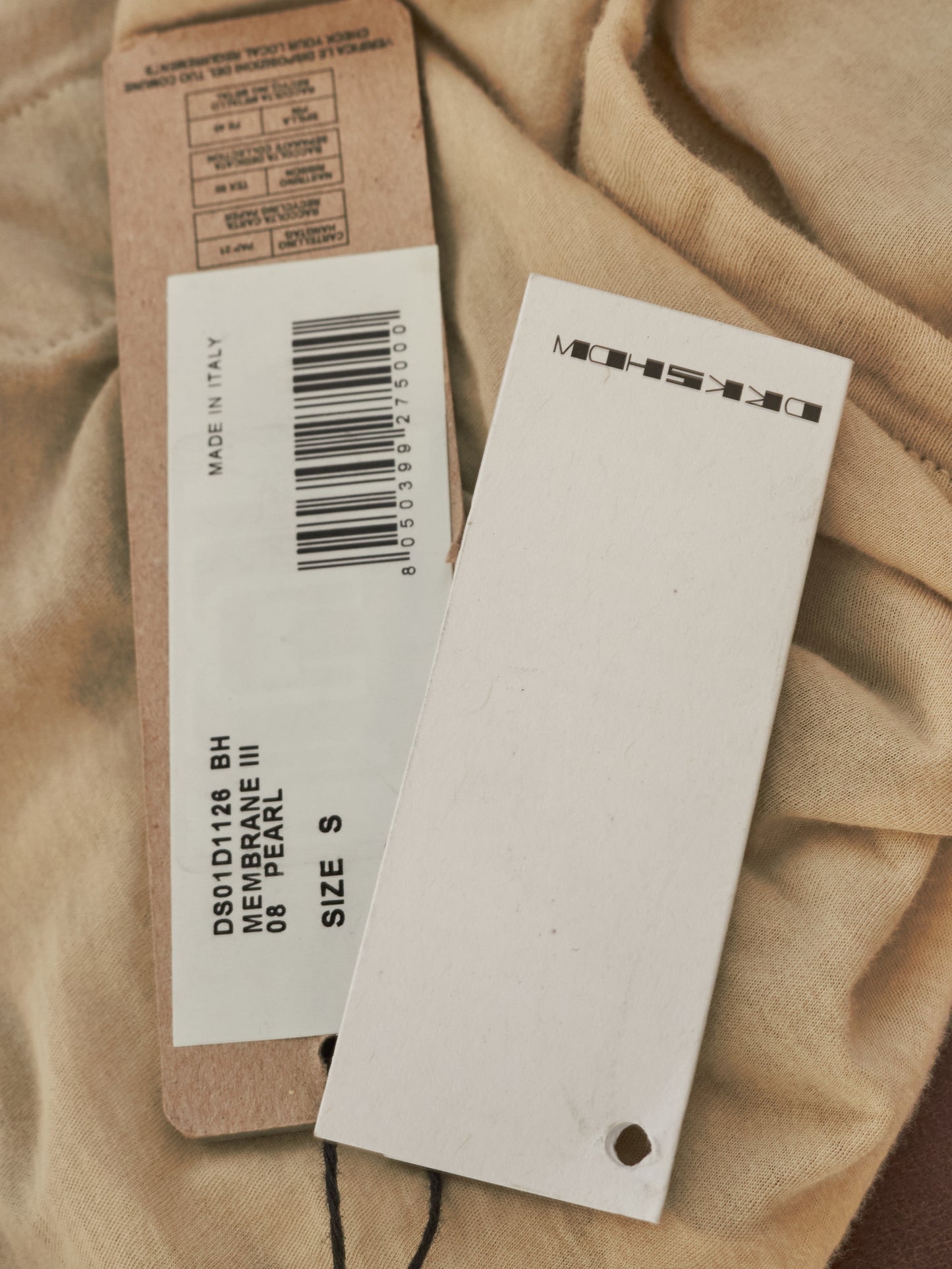 Clothing tags with product information on a beige fabric background