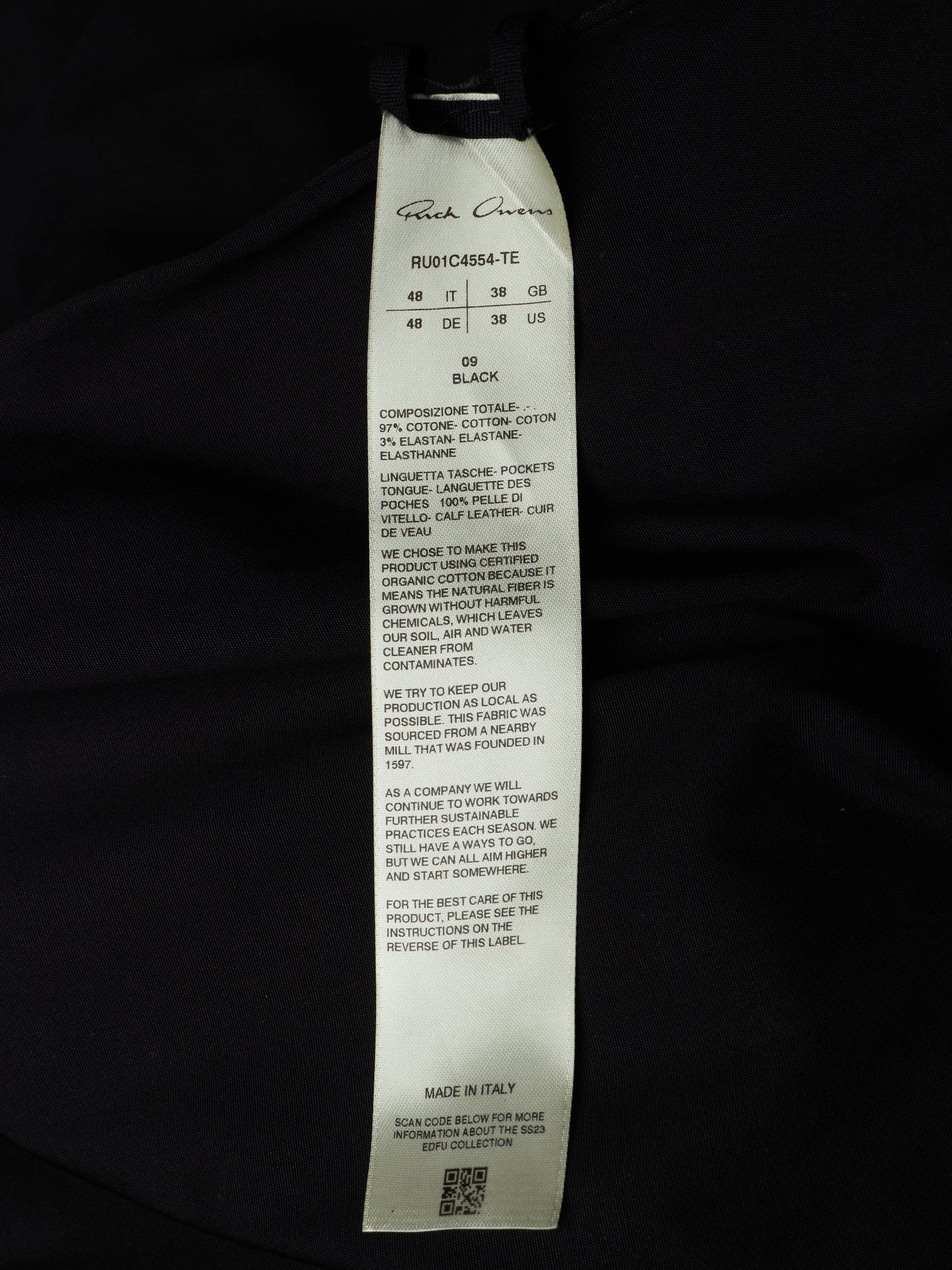 A close-up of a white paper garment tag attached to a black garment, photographed against a black fabric background. The tag shows the brand name 'Ruthless Caviar' and product details including size, color 'Black', and care instructions.