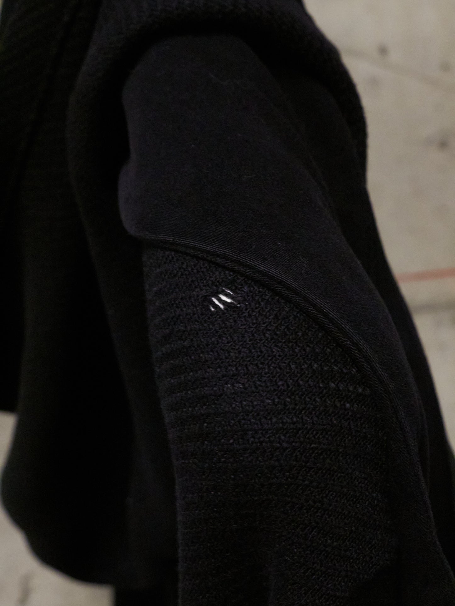 Close-up of a black textured sleeve with a brand logo on a concrete surface.