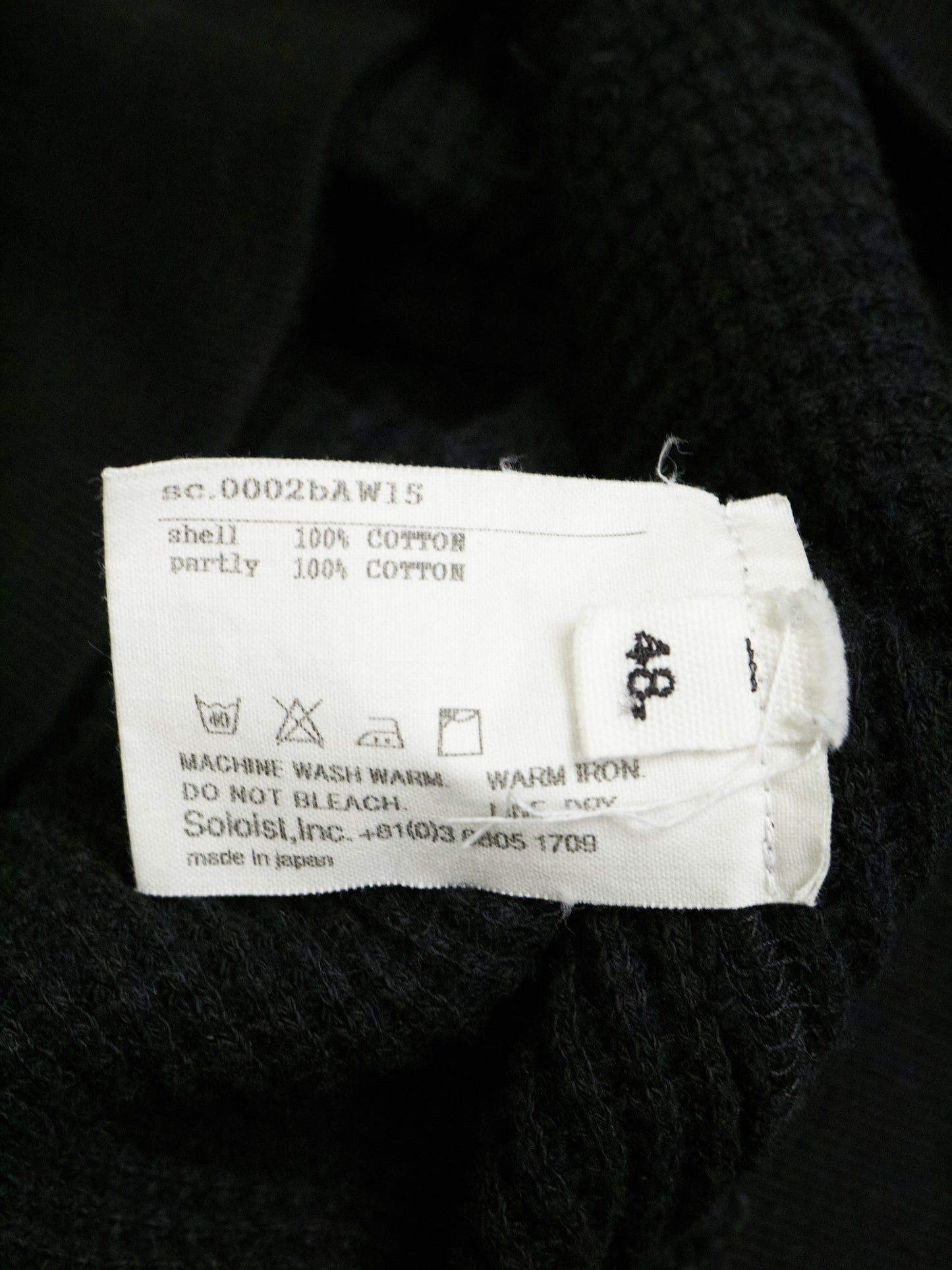 Clothing label on a black garment with text and symbols.