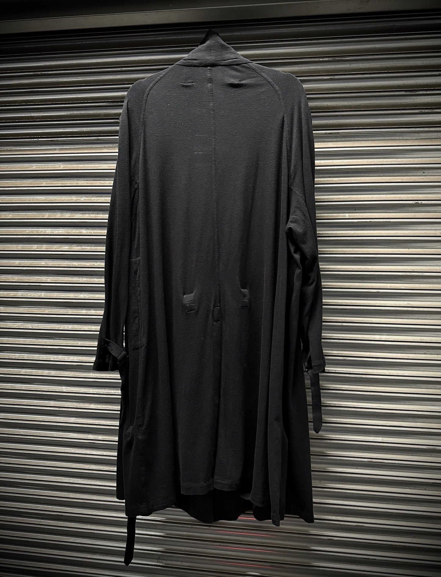 Dark gray coat hanging against a corrugated metal background