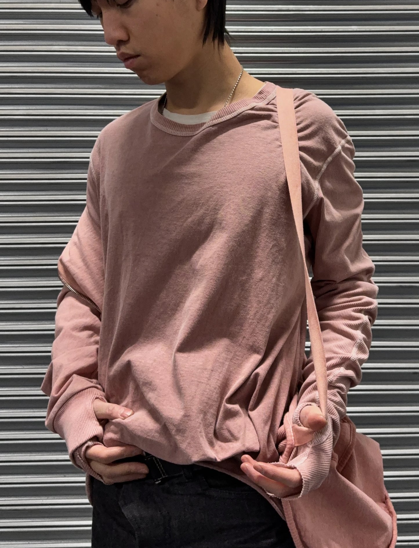 Person wearing a pink long-sleeve shirt holding a pink bag against a metallic shutter background