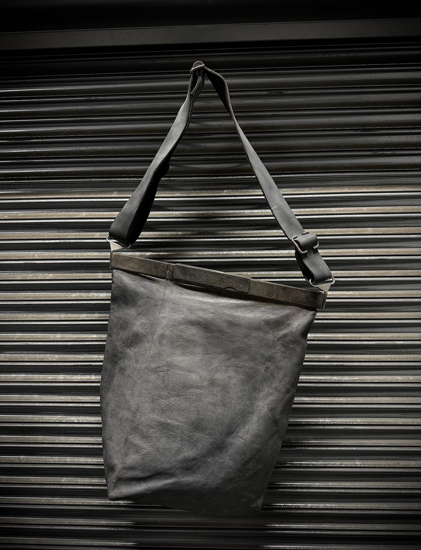 Dark gray leather tote bag with a strap against a metallic background