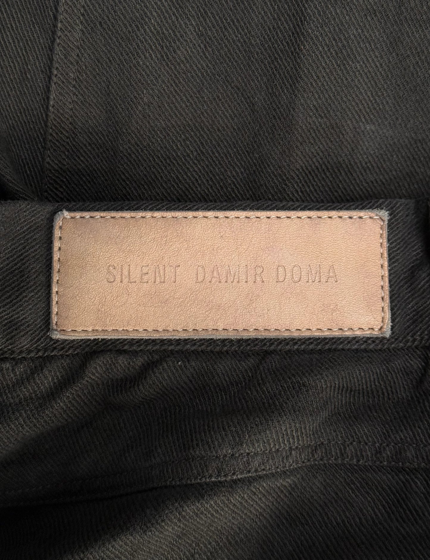 Close-up of a 'Silent Damir Doma' label on black fabric.