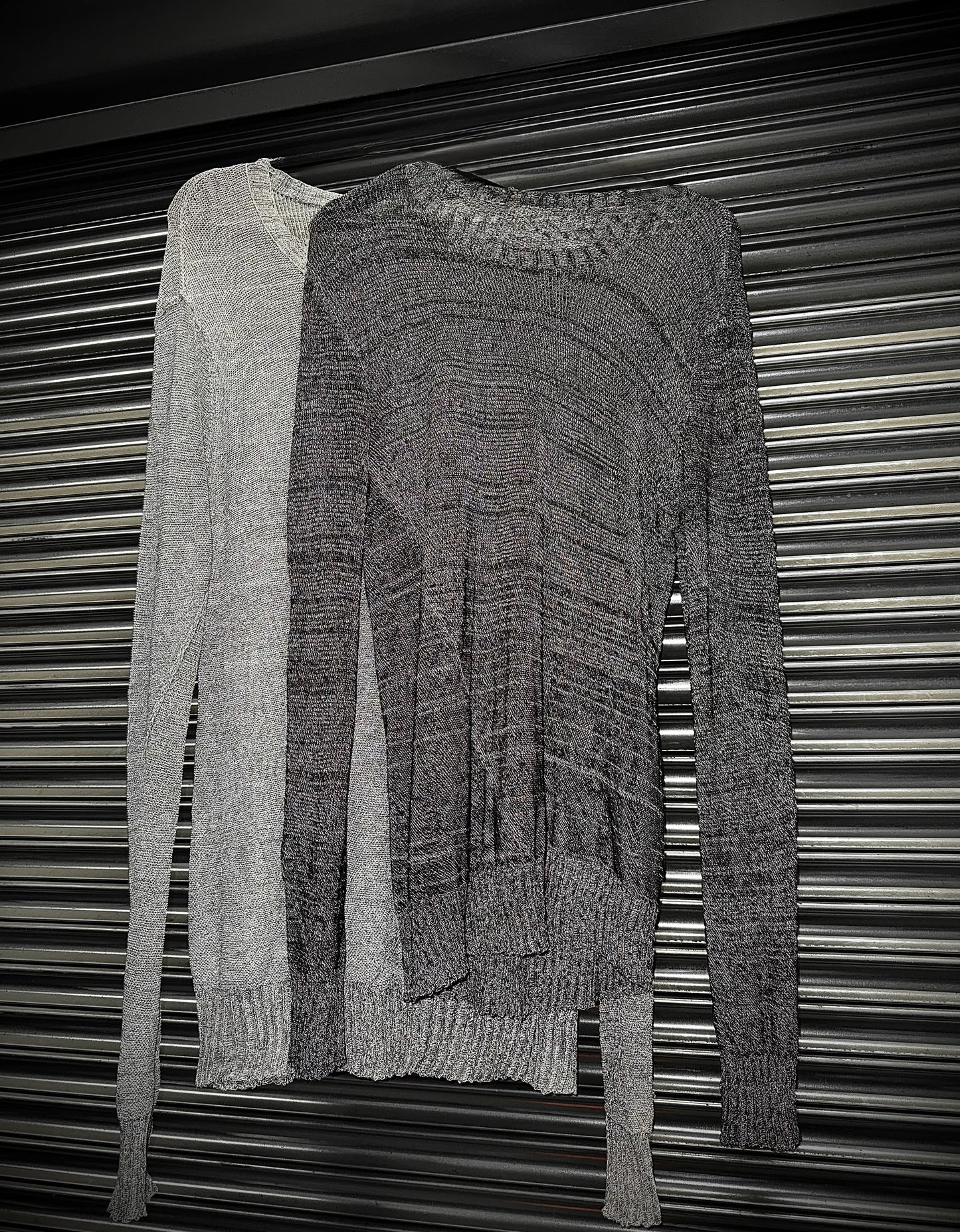 Two knitted sweaters, one gray and one black, draped over a metallic surface.