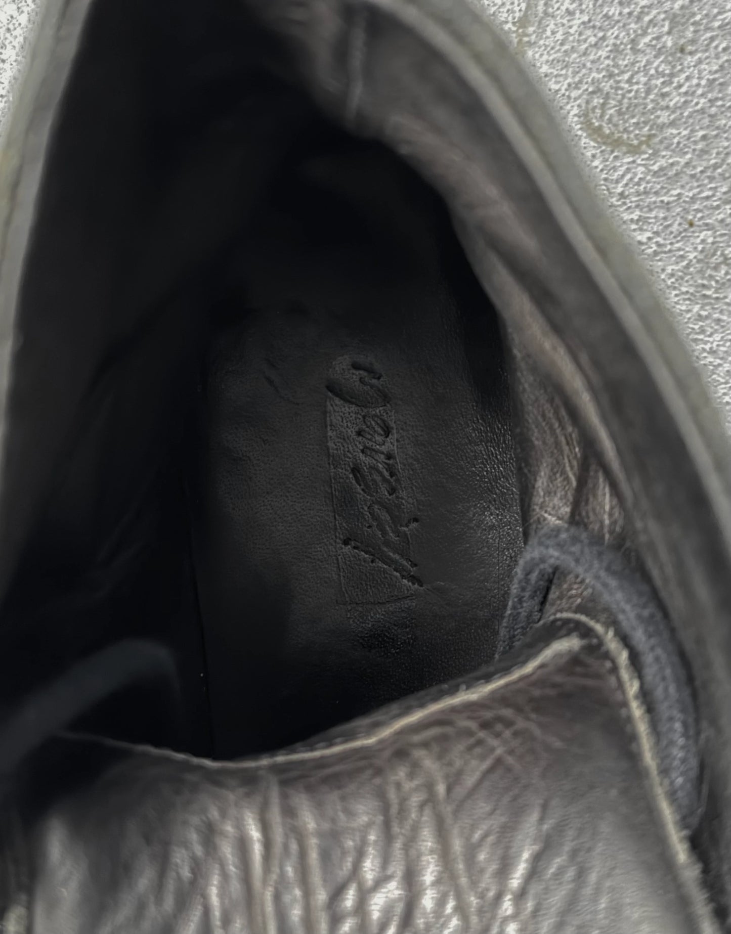 Close-up of a black leather shoe with visible stitching and brand logo.