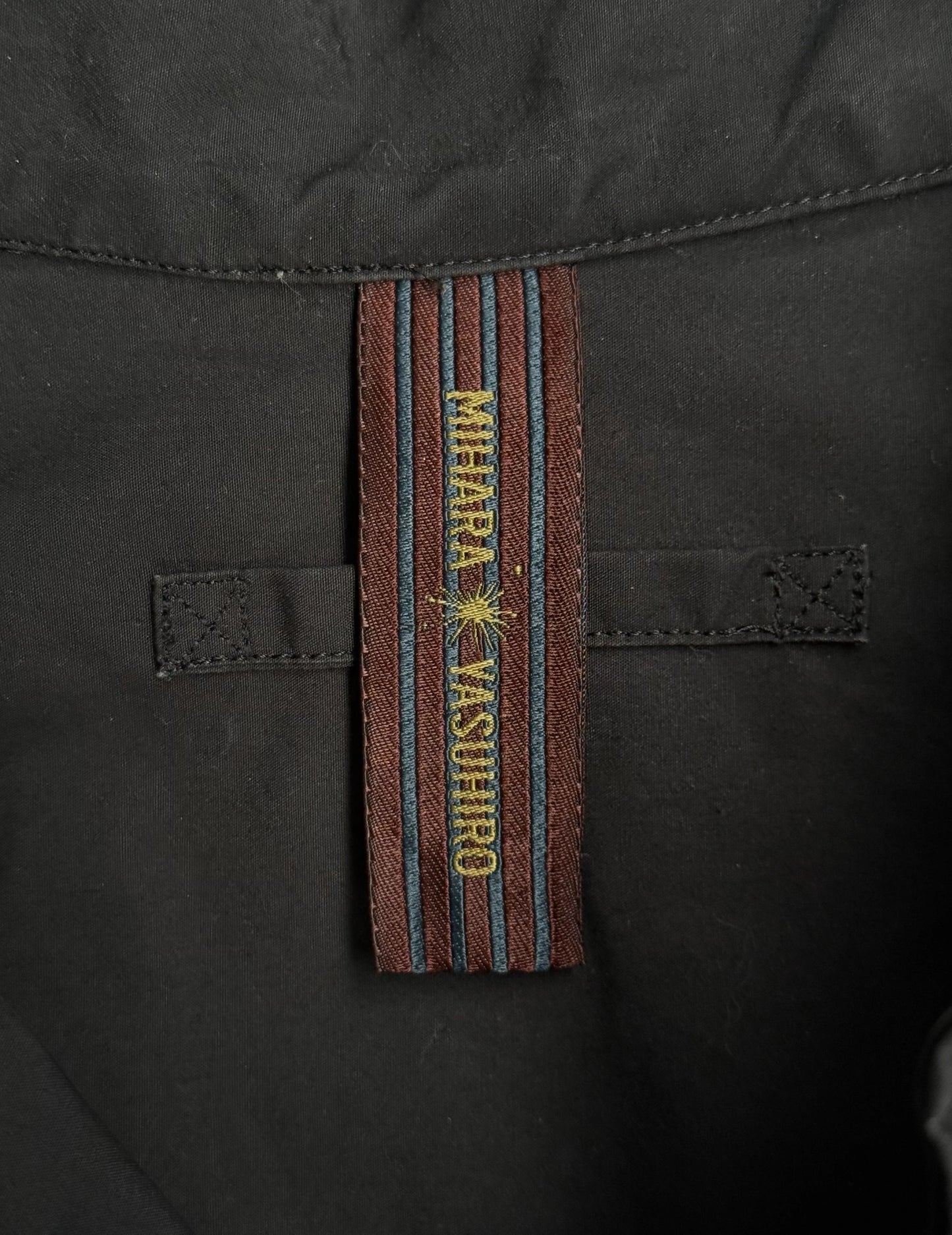 Close-up of a black jacket with a branded strap displaying 'Mihara Yasuhiro'.