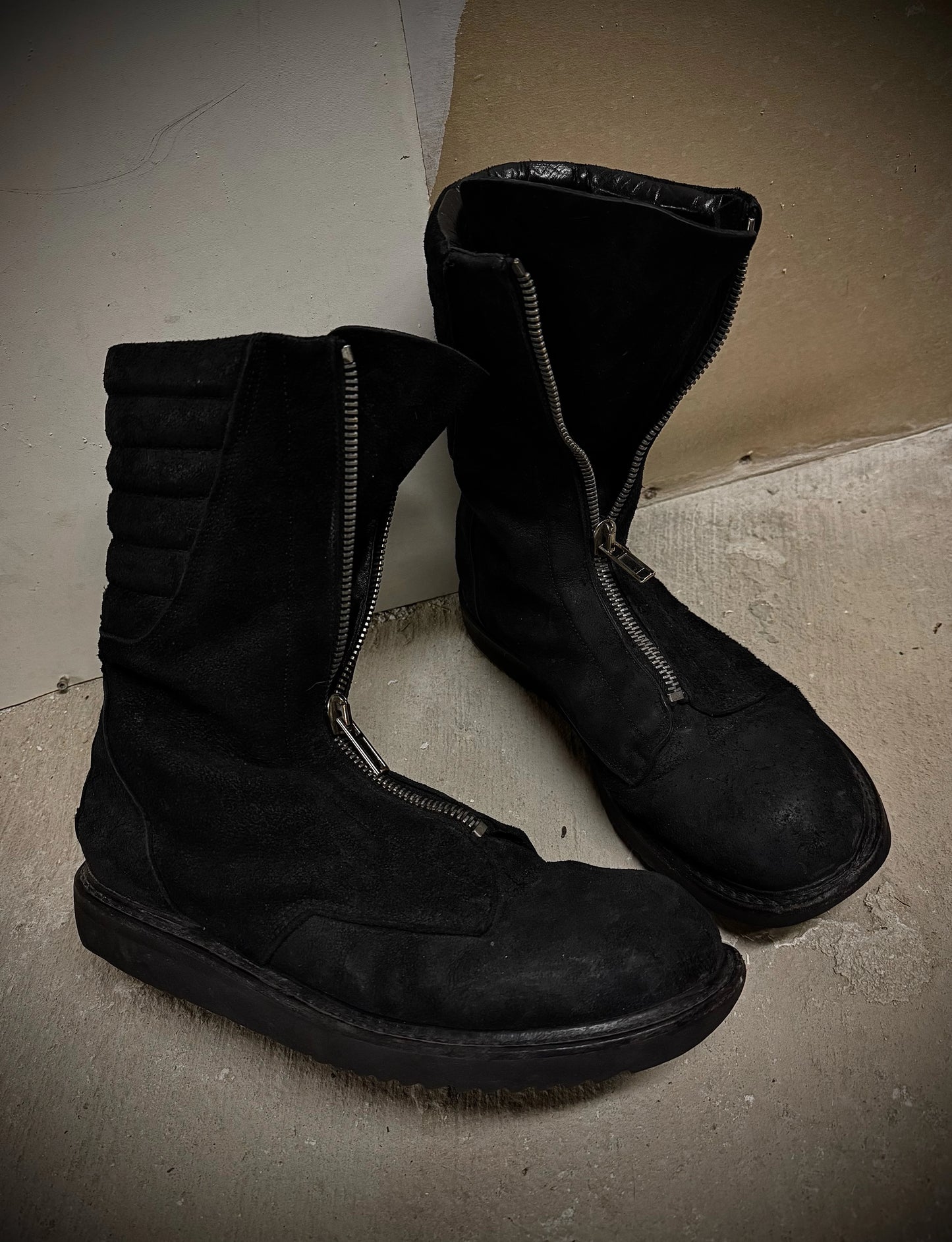 Pair of black boots on a concrete floor with cardboard box in the background