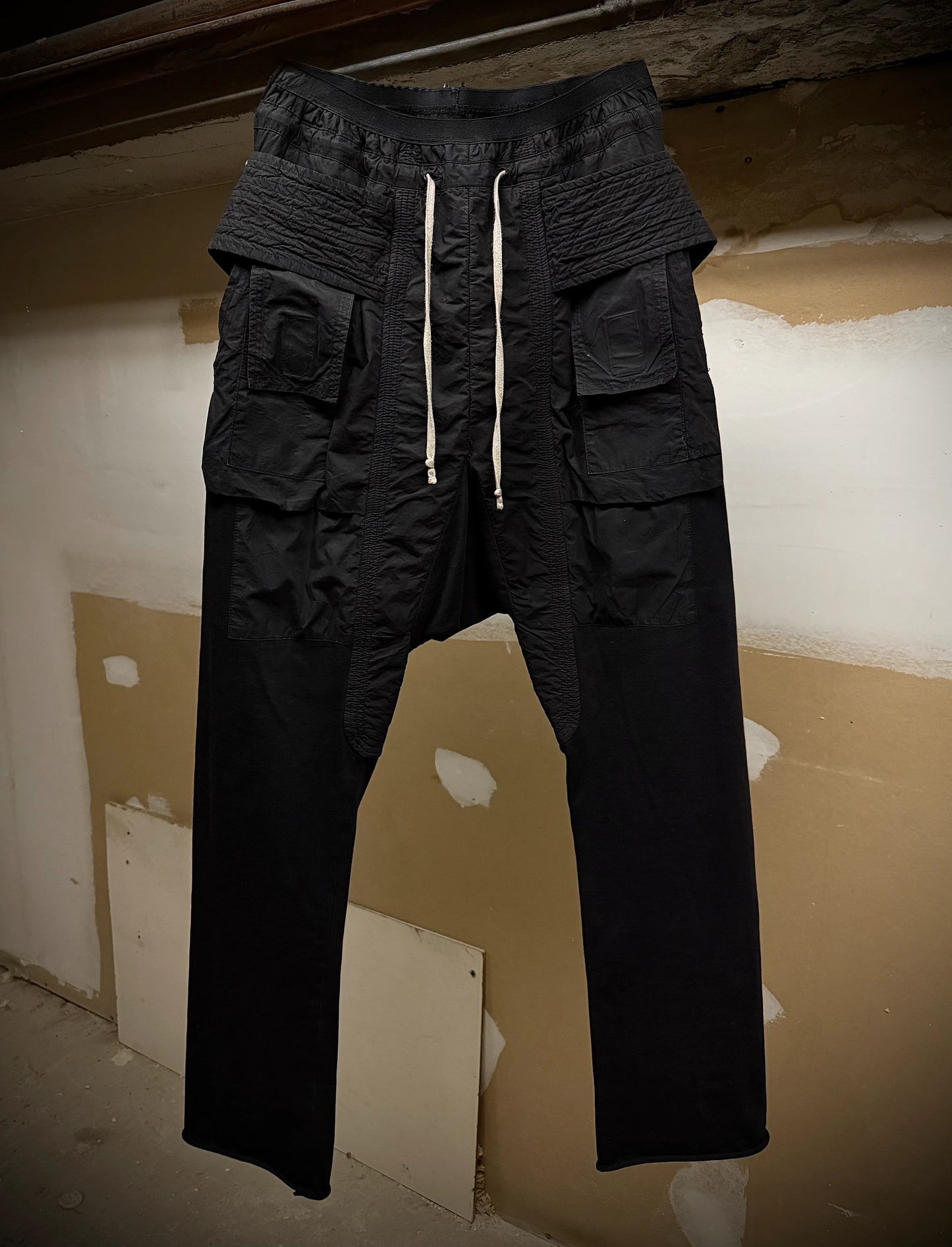 Black cargo pants with multiple pockets and a drawstring on a plain background