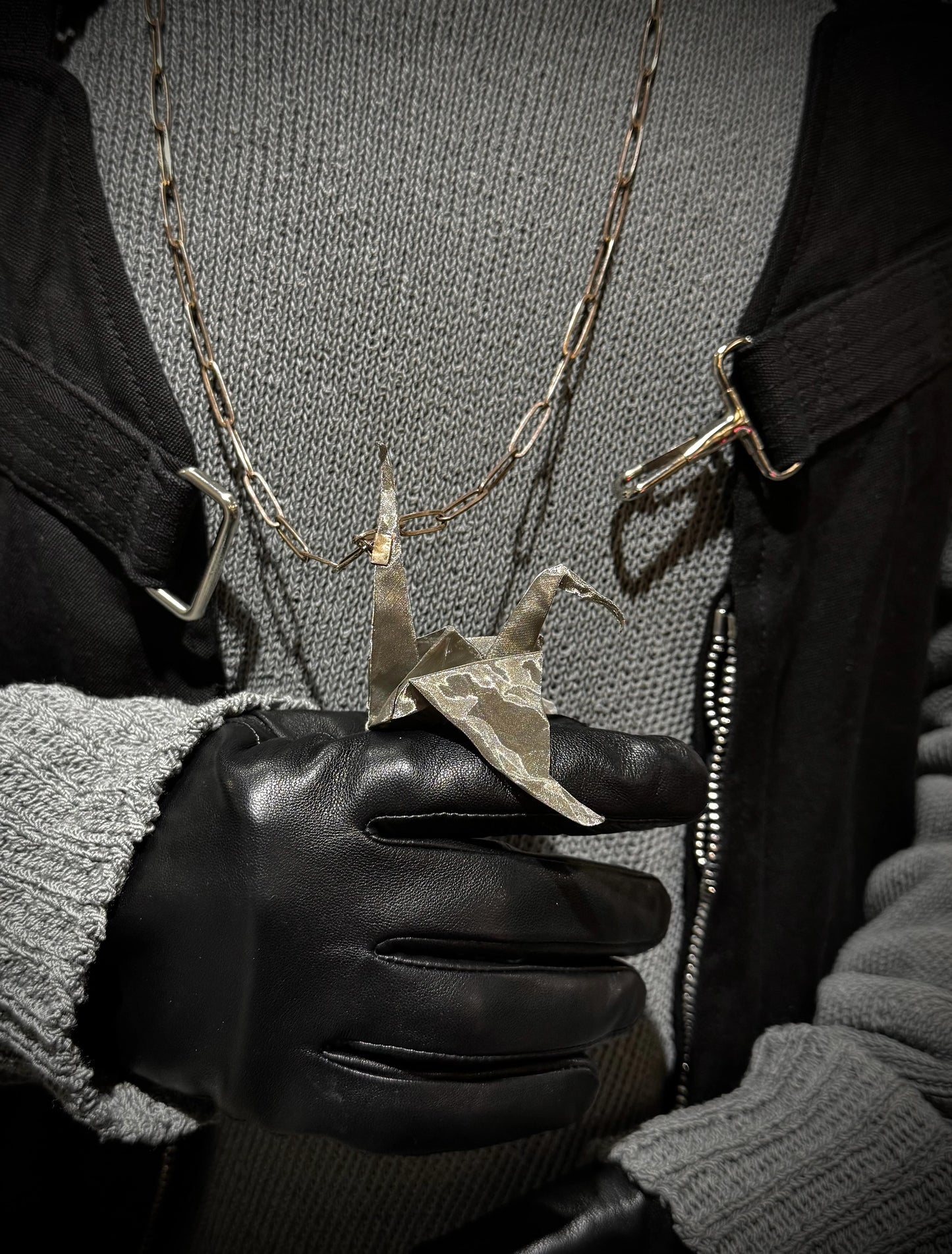 Person wearing a black glove holding a necklace with a unique pendant.