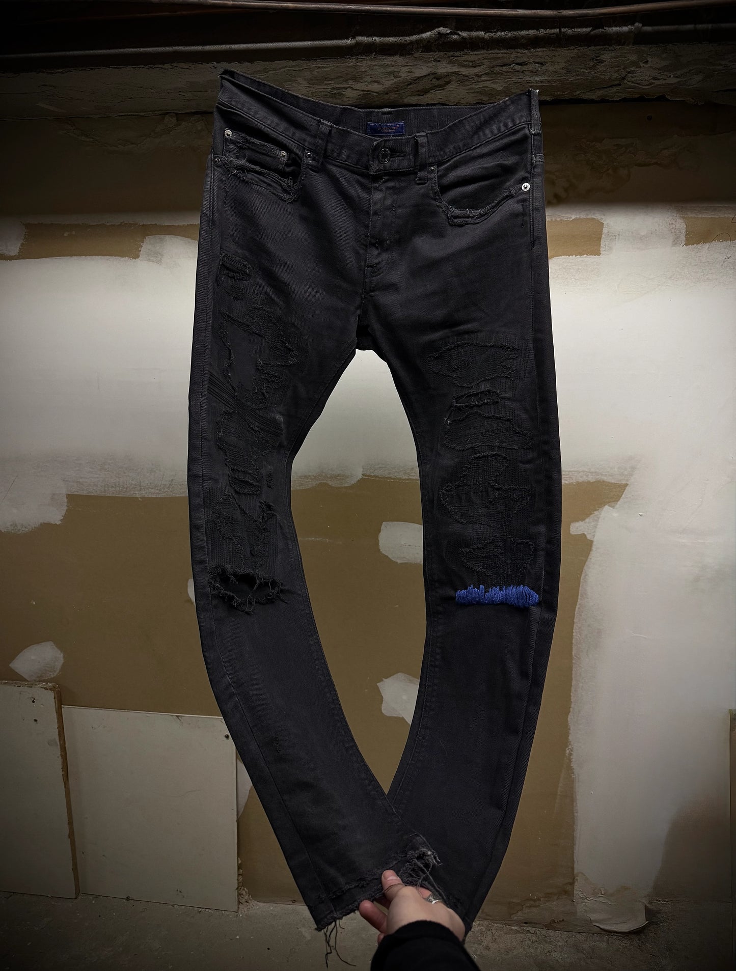 Black distressed jeans held up against a plain background