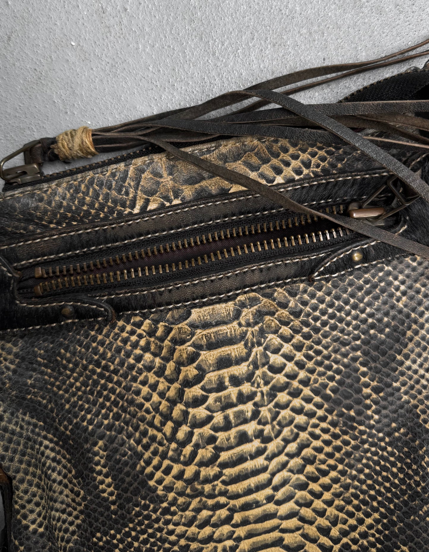 Close-up of the Kyoji Maruyama Early 00s Yellow Crocodile Embossed Leather Side Bag, featuring textured leather, a visible zipper, and dark fringe detail on a light gray surface.