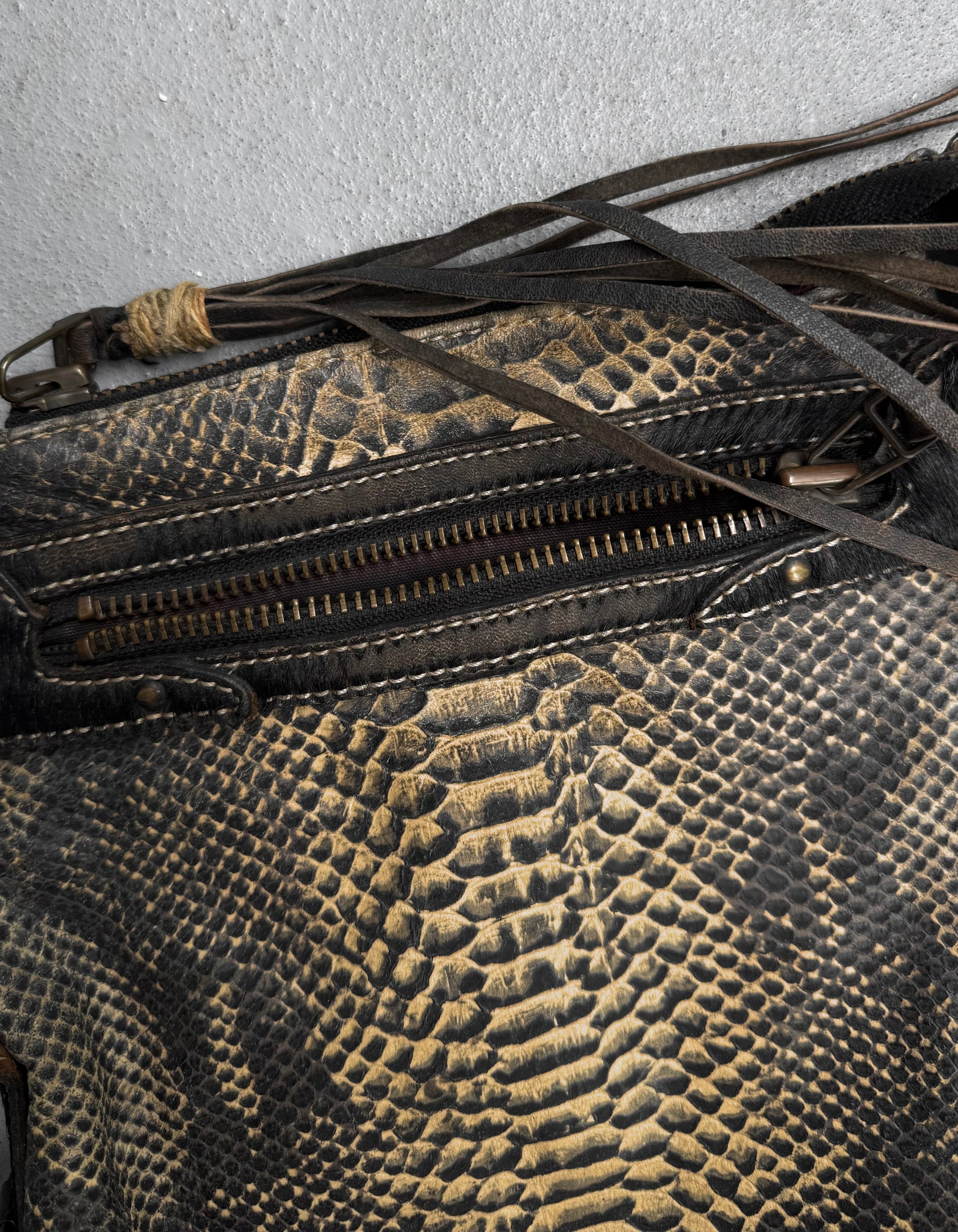 Close-up of the Kyoji Maruyama Early 00s Yellow Crocodile Embossed Leather Side Bag, featuring textured leather, a visible zipper, and dark fringe detail on a light gray surface.