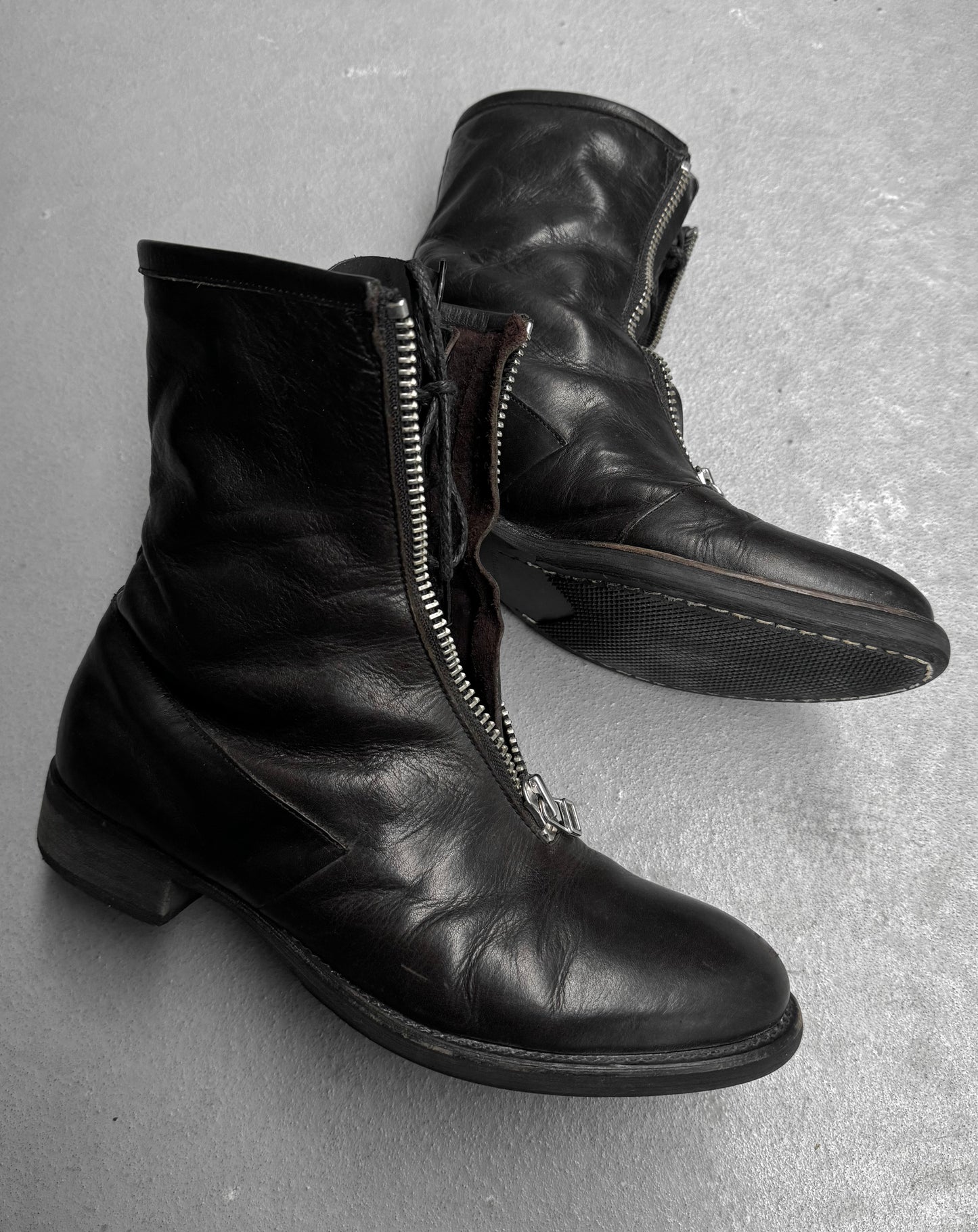 Pair of black leather boots with zippers on a gray surface