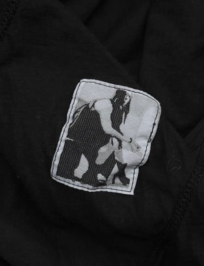 The Rick Owens DRKSHDW AW24 “PORTERVILLE” Geometric Level Long-sleeves features a black and white patch on black fabric, showing a stylized figure bending toward a small animal in pixelated, minimalist fashion.