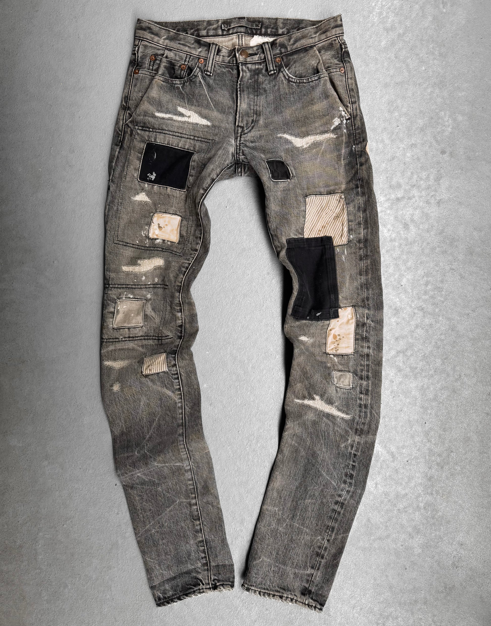 The Mihara Yasuhiro AW10 Double-pockets Repair Patchwork Selvedge Denim features a distressed gray wash, black, beige, and striped fabric patches, visible wear, frayed edges, and worn spots—showcasing bold Japanese streetwear style.