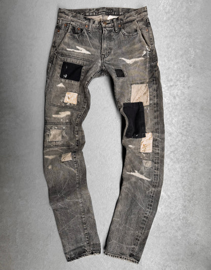 The Mihara Yasuhiro AW10 Double-pockets Repair Patchwork Selvedge Denim features a distressed gray wash, black, beige, and striped fabric patches, visible wear, frayed edges, and worn spots—showcasing bold Japanese streetwear style.