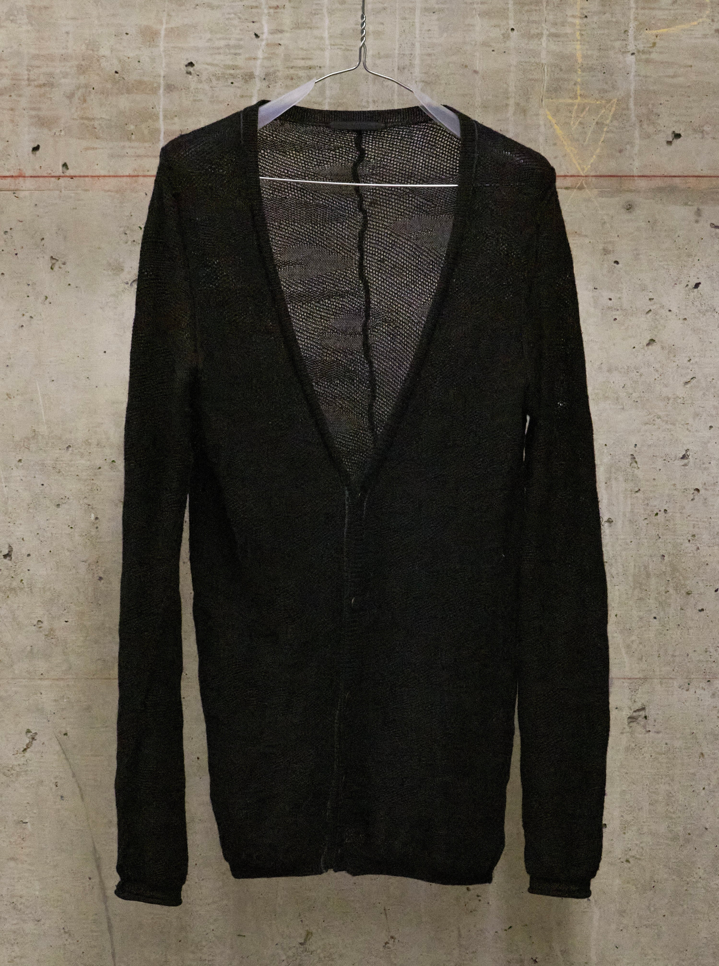 Black cardigan on a hanger against a textured beige wall