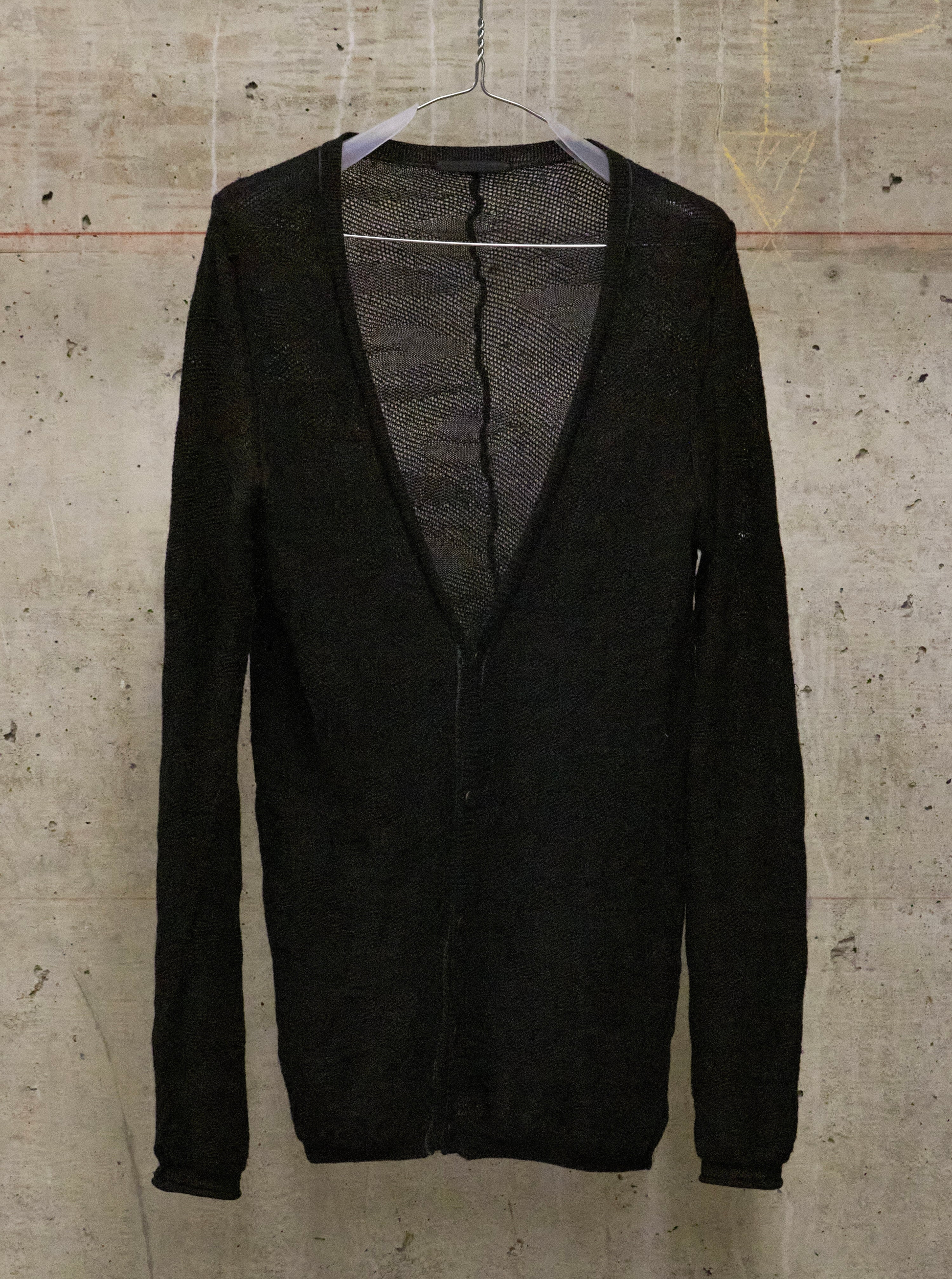 Black cardigan on a hanger against a textured beige wall
