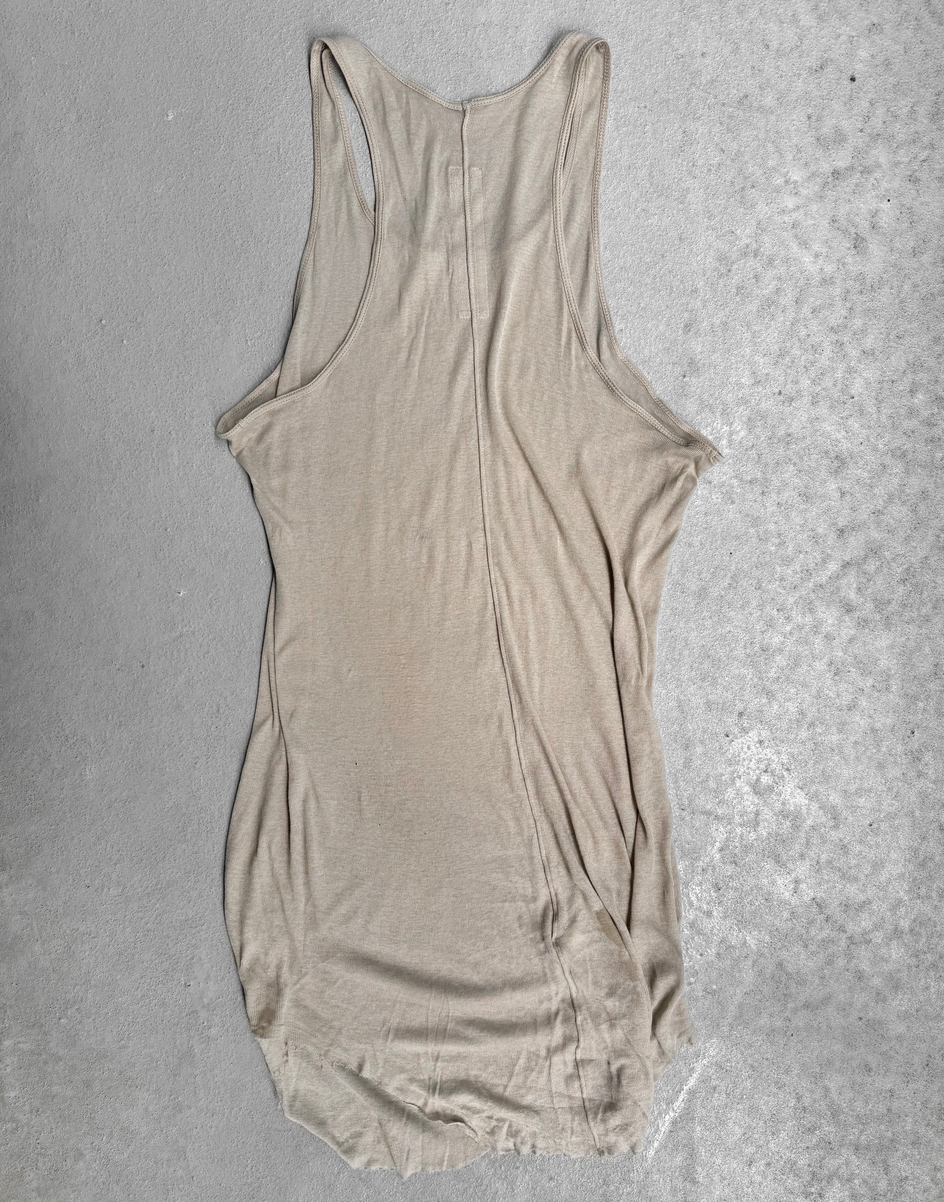 The Rick Owens SS24 “LIDO” Pearl Sheer D-Flap Tank Top, featuring a racerback and sculptural silhouette, is displayed flat on a light gray concrete surface. The fabric is slightly wrinkled with uneven edges.