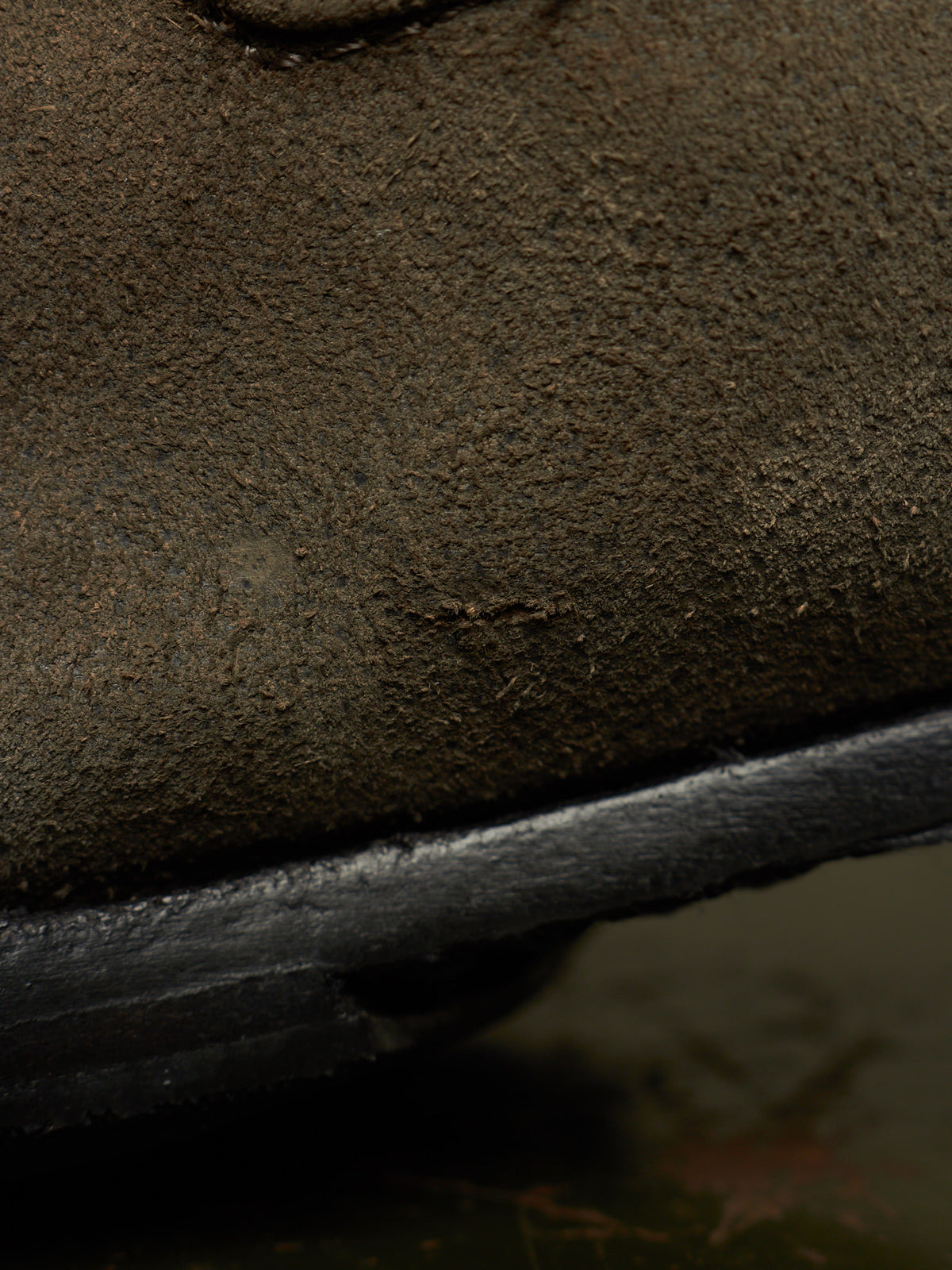 Close-up detail of a dark brown suede or nubuck shoe upper with a black rubber sole edge.