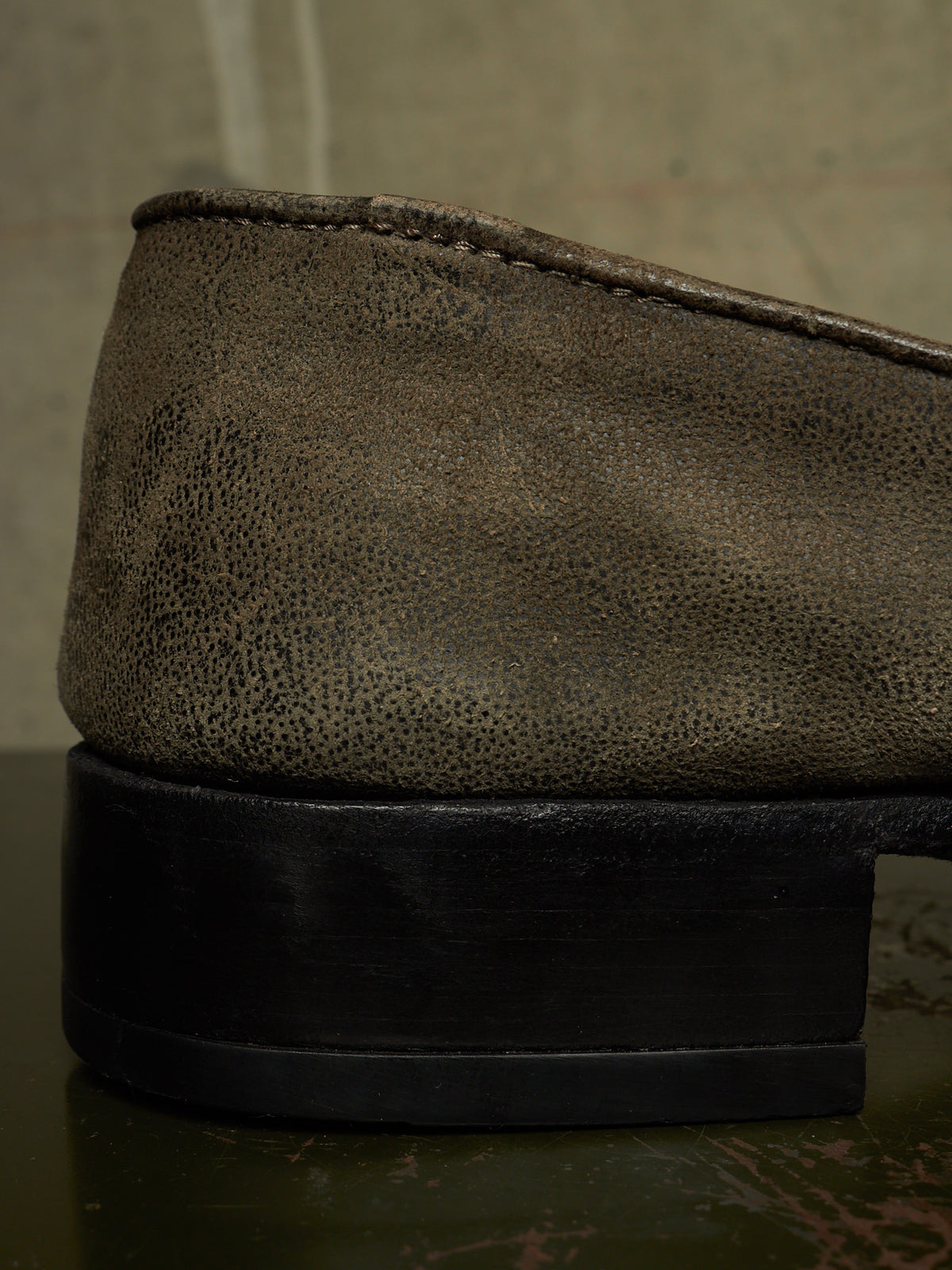 Close-up of the side of a dark brown textured leather shoe with a chunky black sole, resting on a dark reflective surface.