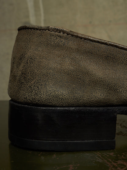 Close-up of the side of a dark brown textured leather shoe with a chunky black sole, resting on a dark reflective surface.