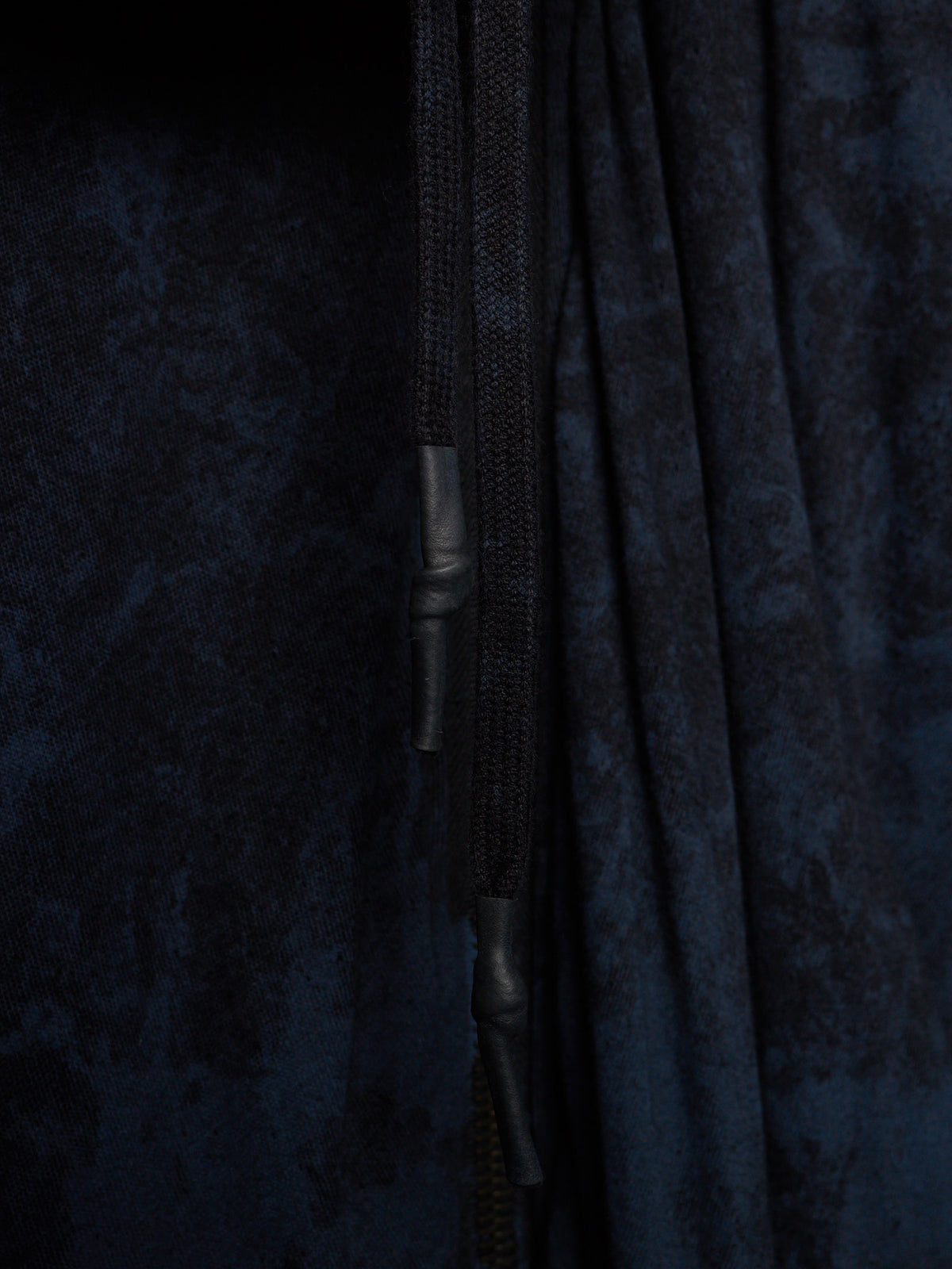 Close-up of a dark navy blue textured fabric garment with a black drawstring and black zipper pull.