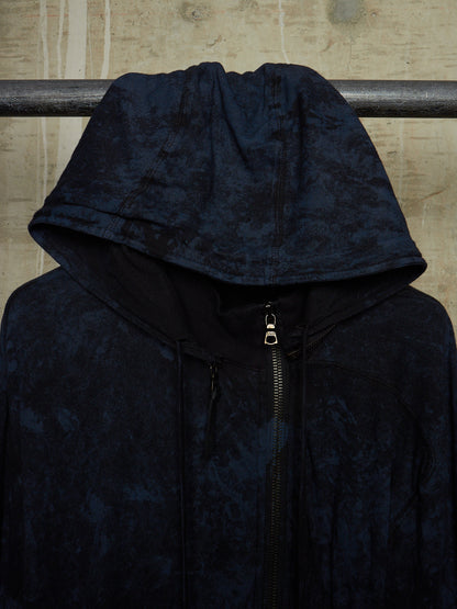 A dark navy hooded jacket with a textured, marbled pattern, hanging on a metal rack against a textured beige wall.