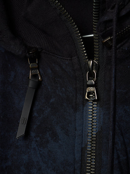 Close-up of a dark navy hooded jacket with a black zipper and a black pull tab featuring a small white logo, set against a dark textured fabric background.