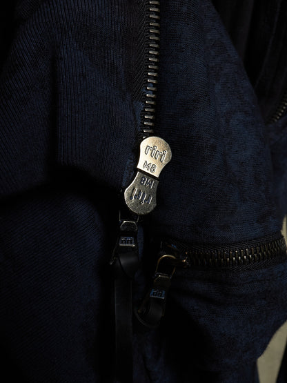 Close-up of a dark navy textured zippered garment with a silver-tone metal zipper pull engraved with 'mini MB' and 'BAH JUD'.