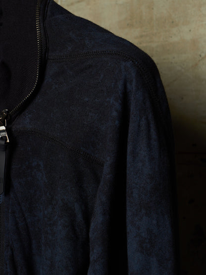 Close-up of a dark navy textured zip-up jacket with a ribbed collar and a silver zipper pull, set against a warm, neutral background.