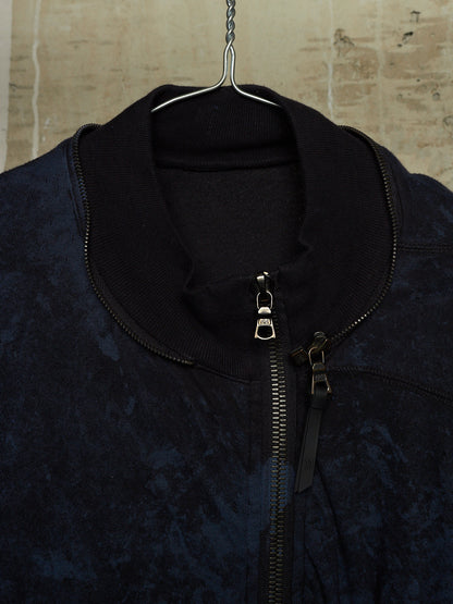 A close-up of a dark navy blue textured zip-up jacket hanging on a metal hanger against a light beige stone wall.