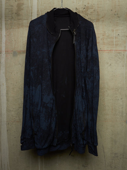 A dark navy blue lightweight jacket with a subtle marbled pattern, hanging open over a black top against a textured concrete wall.