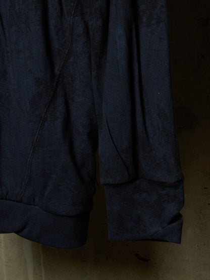 Close-up of a dark navy blue textured fabric garment, showing the cuff of a sleeve and the side seam against a dim, warm-toned background.