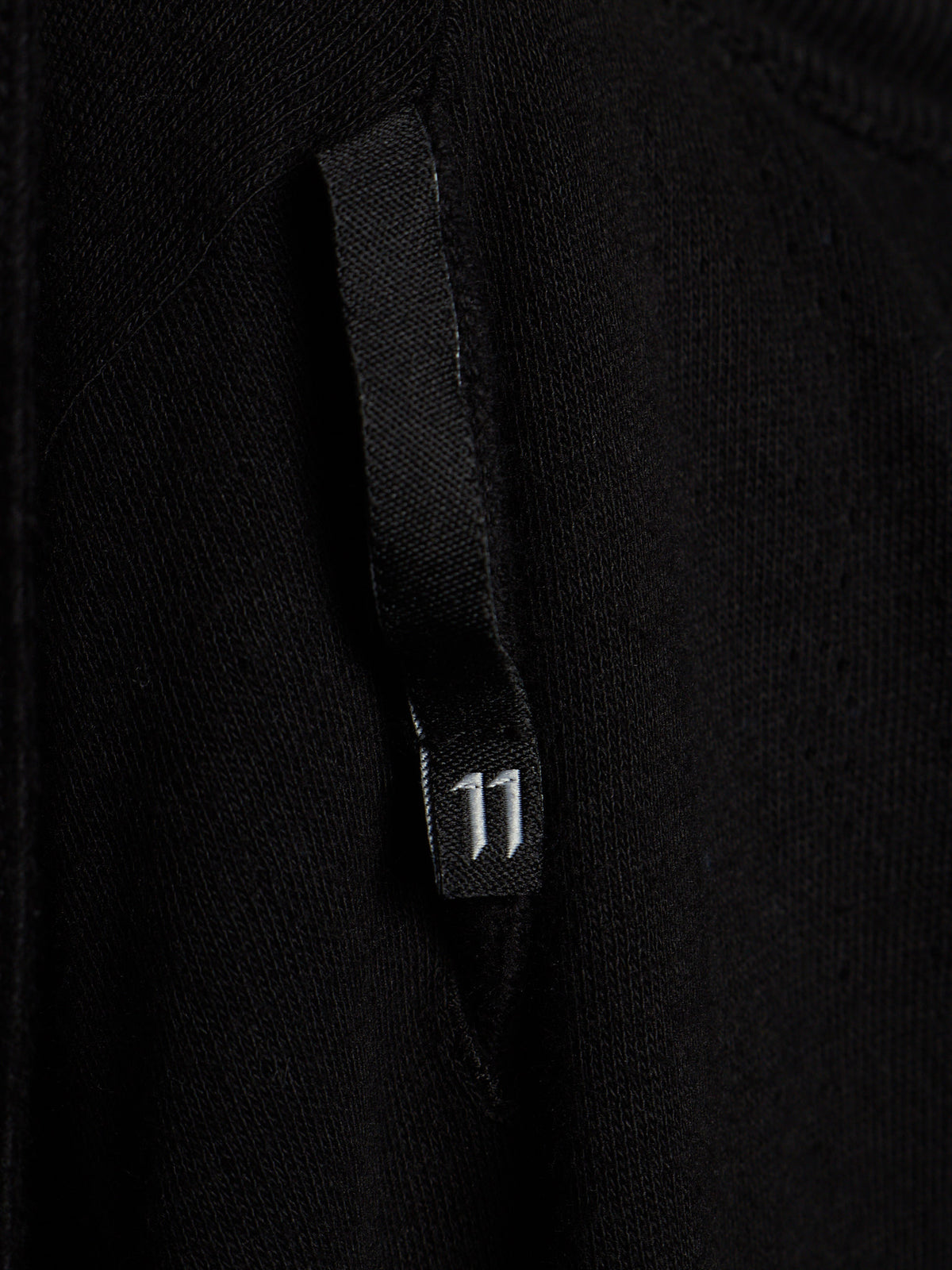 Close-up of a black knit garment featuring a black fabric tab with a small white '11' printed on it.