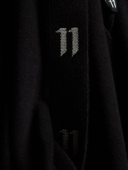 Close-up of a black knit garment featuring a large white stylized '11' logo on the sleeve, with a smaller matching logo visible near the collar.