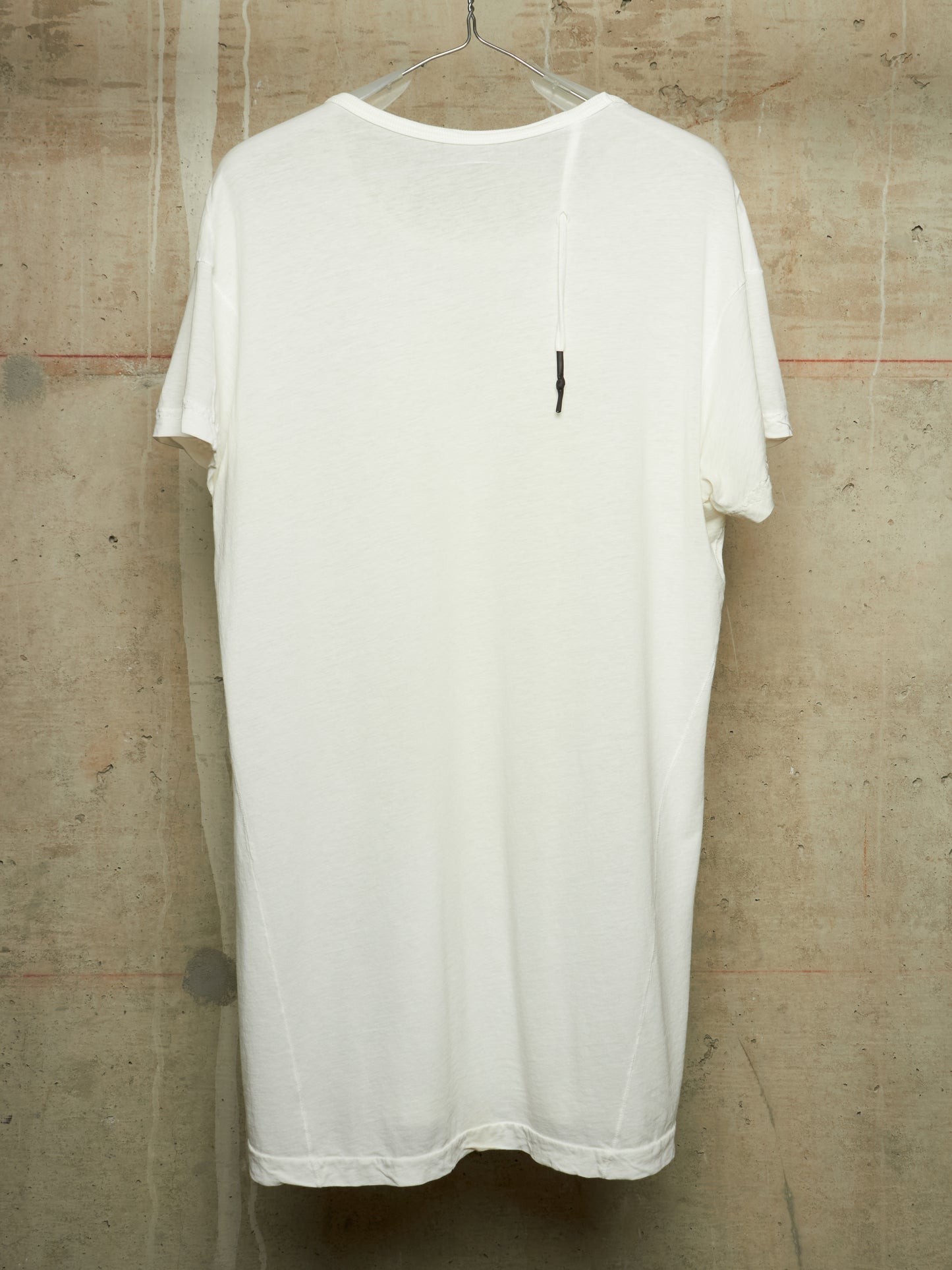 A white short-sleeve t-shirt hanging on a clear plastic hanger against a textured concrete wall.