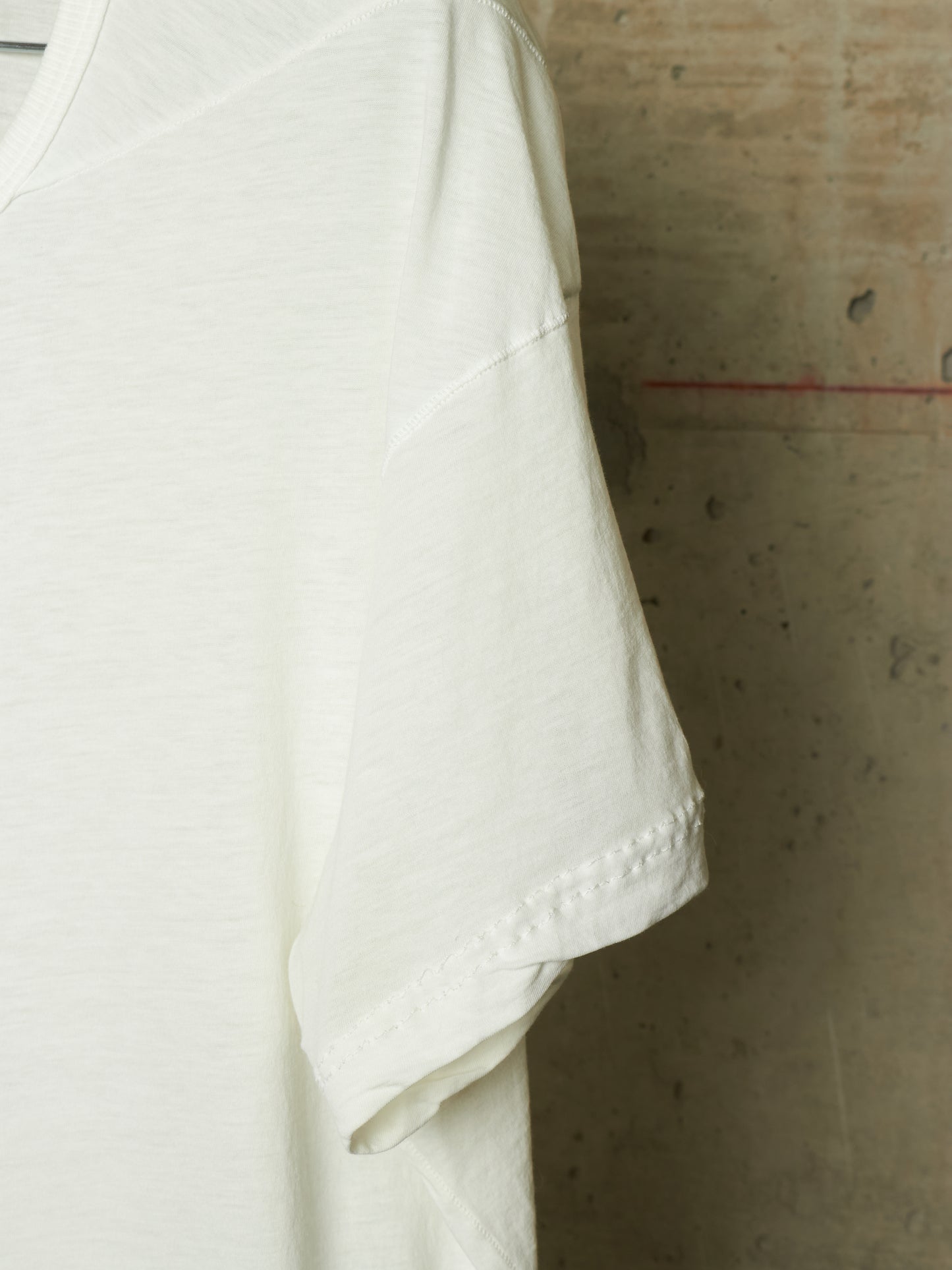 Close-up of a white short-sleeve t-shirt hanging against a textured concrete wall.