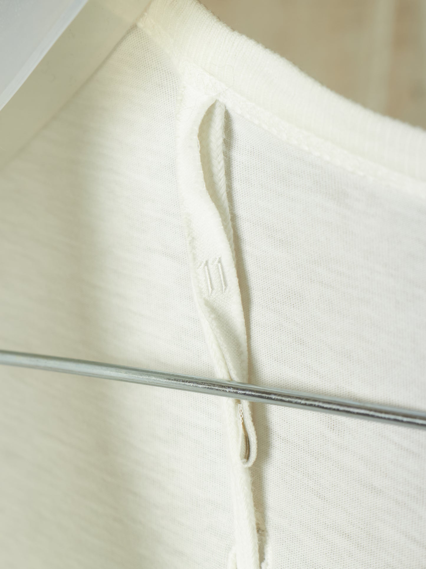 Close-up of a cream-colored ribbed knit garment, likely a hoodie or sweatshirt, showing the drawstring loop and ribbed texture.